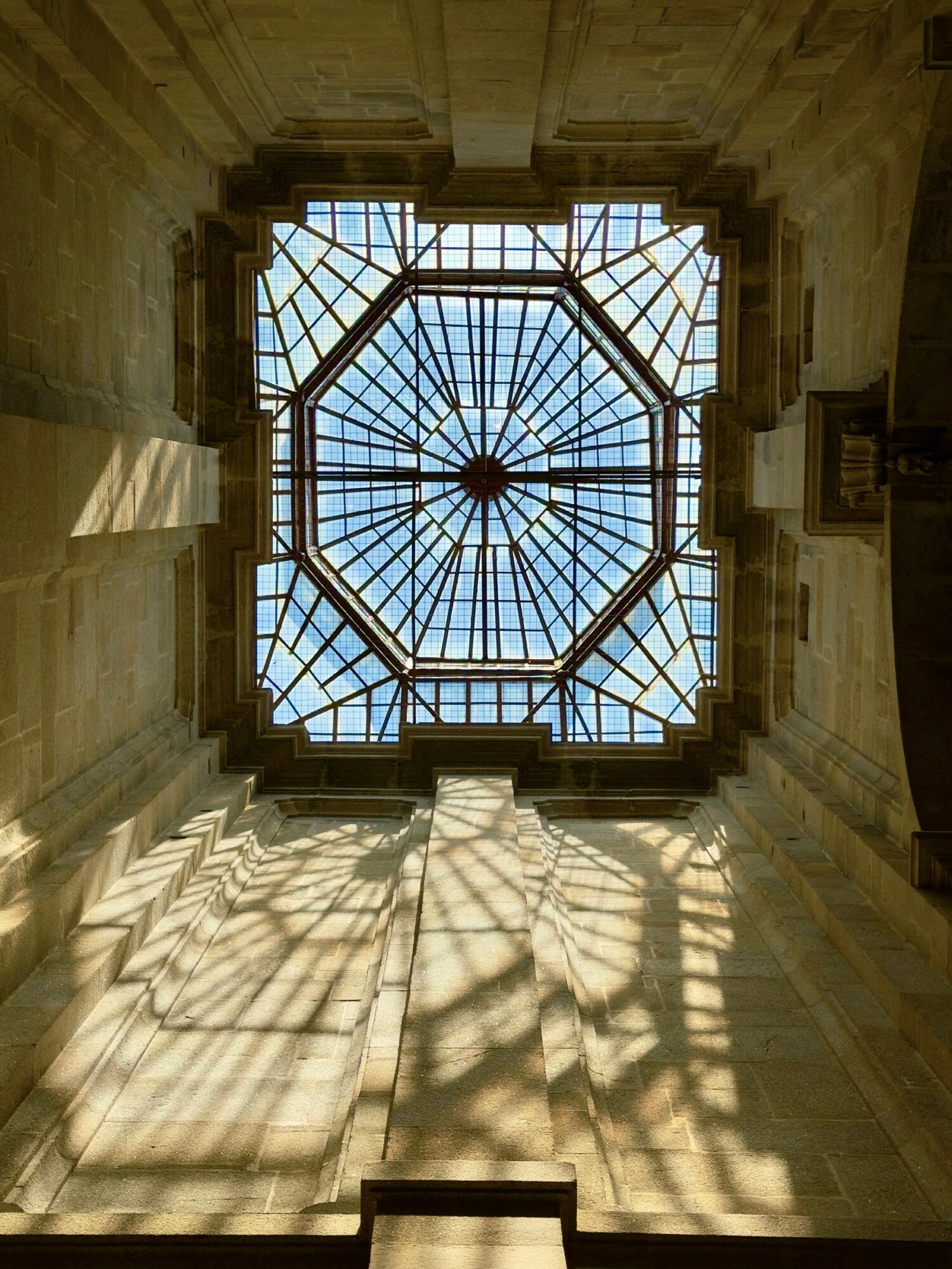 View of a glass ceiling with a geometric pattern, casting shadows on the surrounding stone walls.
