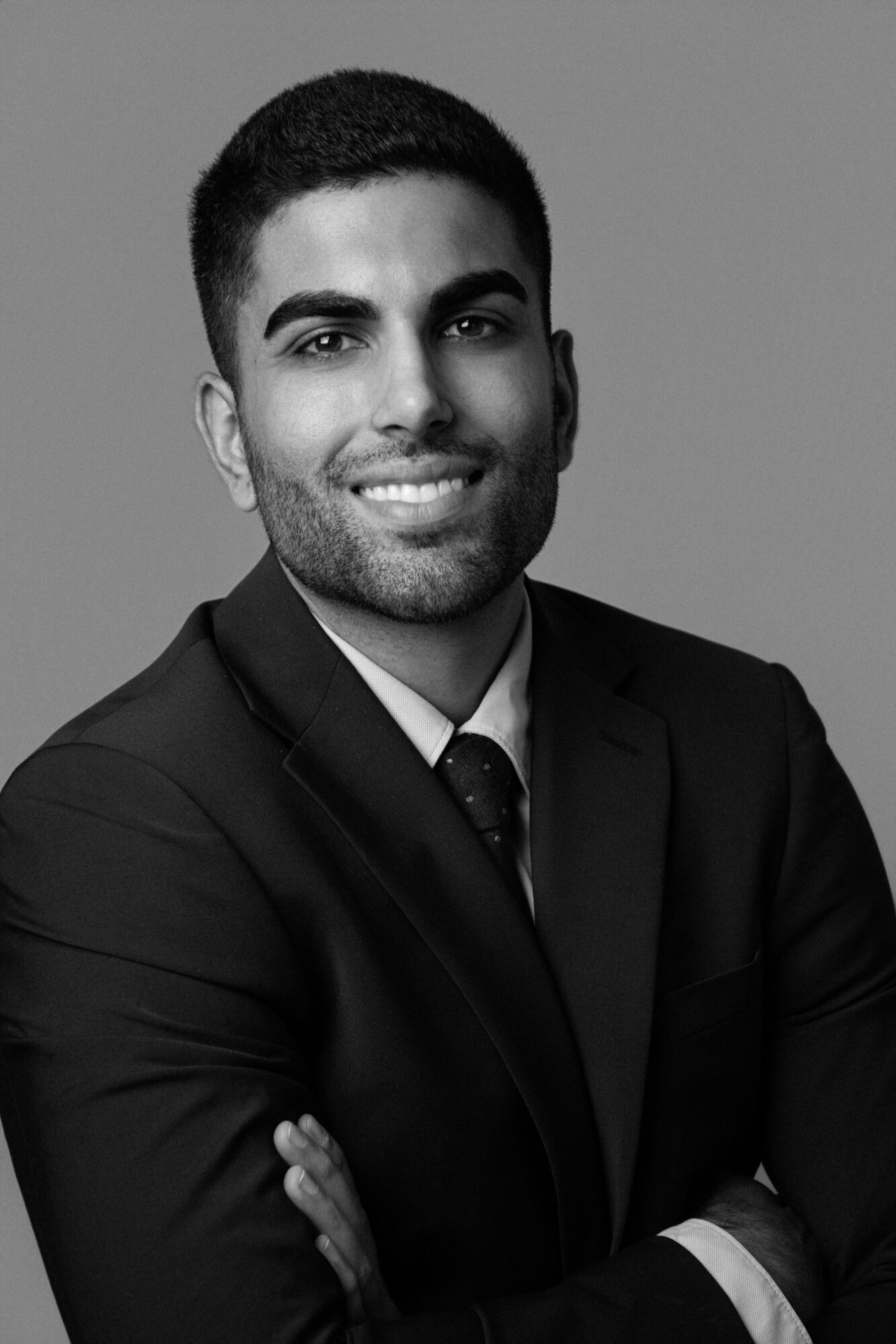 Portrait of a smiling man in a suit with arms crossed, facing forward.