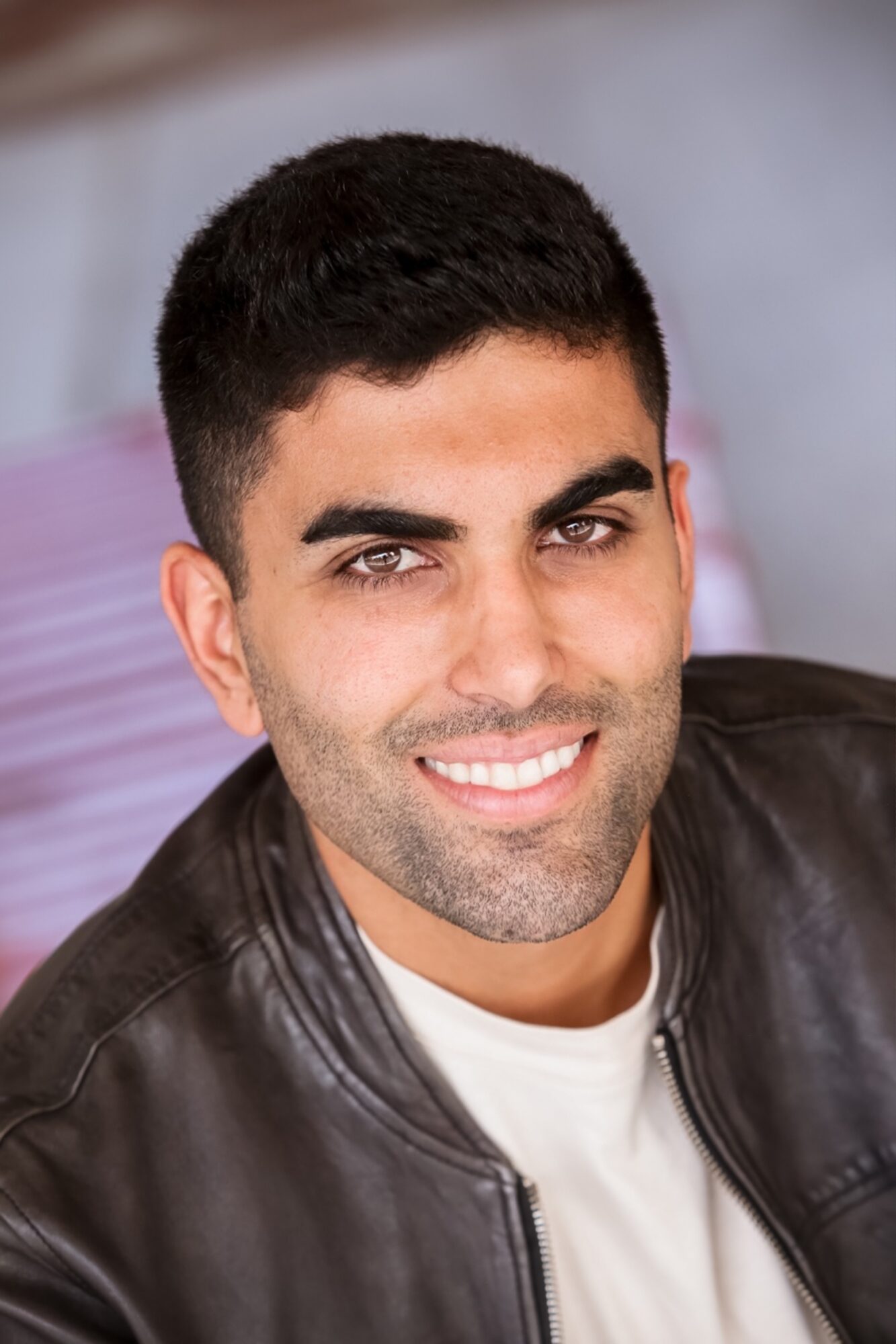 Close-up of a smiling man with short dark hair, wearing a black leather jacket and white shirt.