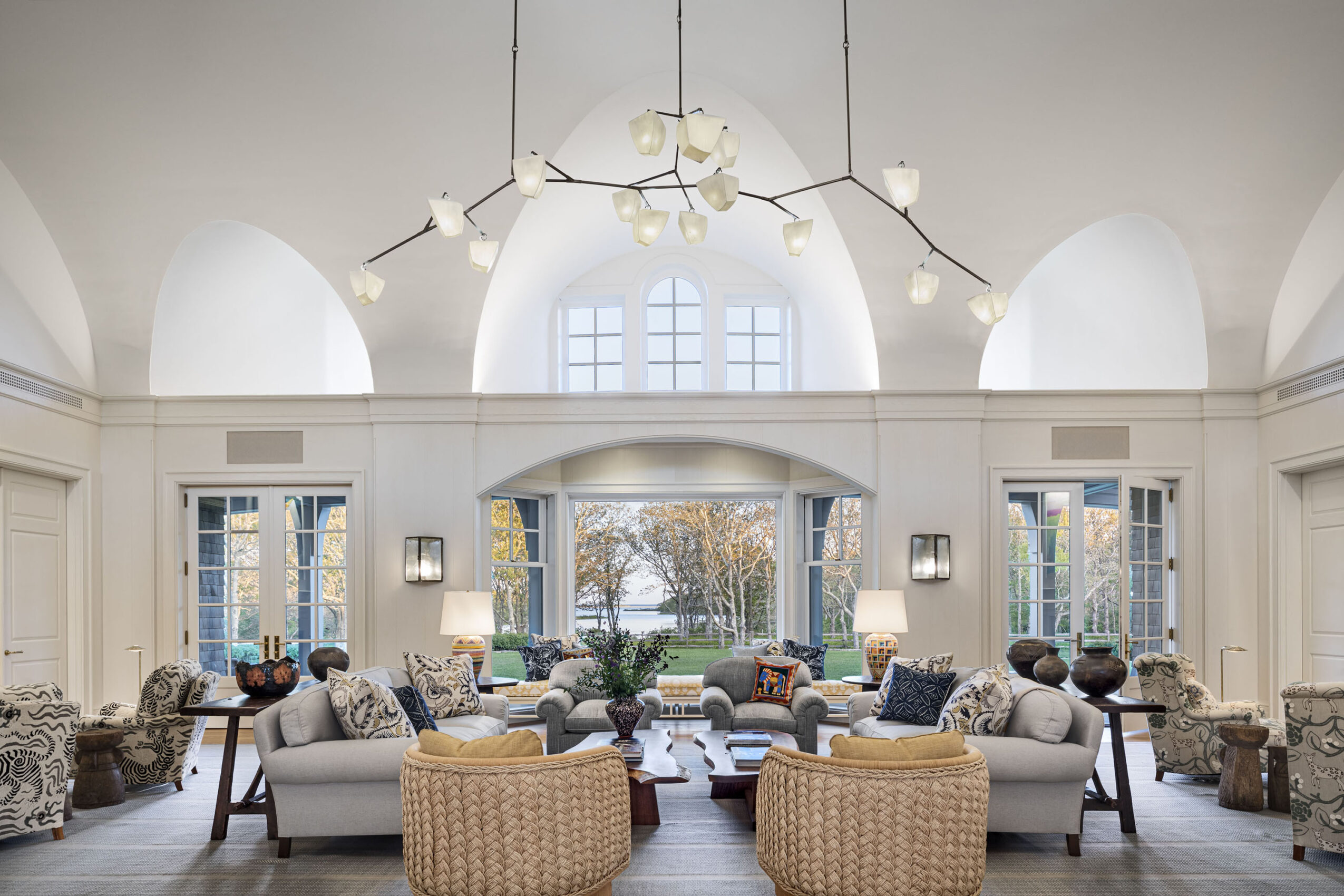 Elegant room with large windows, a chandelier, and comfortable seating arranged around a central table.