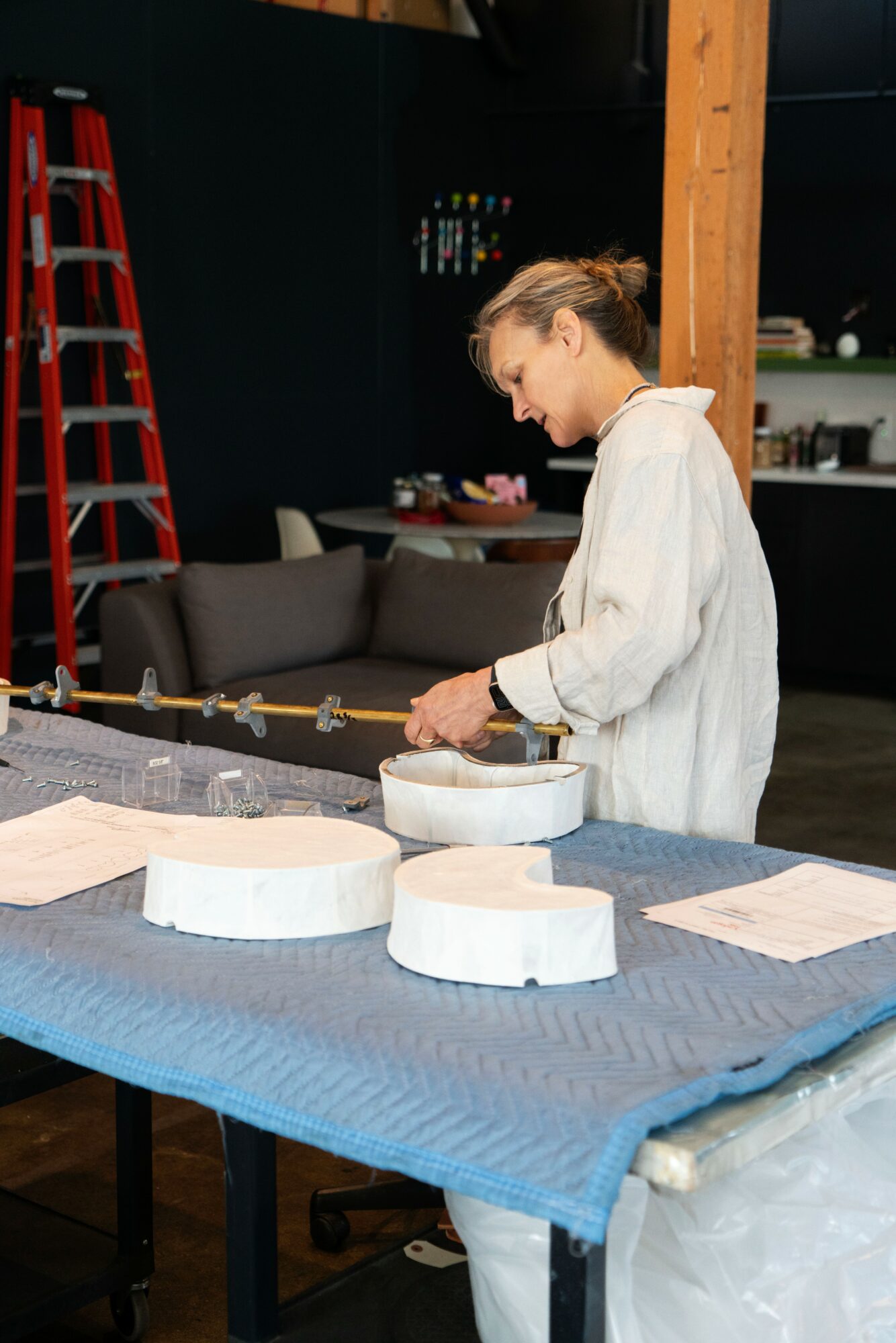 Person in white coat working at a table with circular objects, in a room with a ladder and shelves.