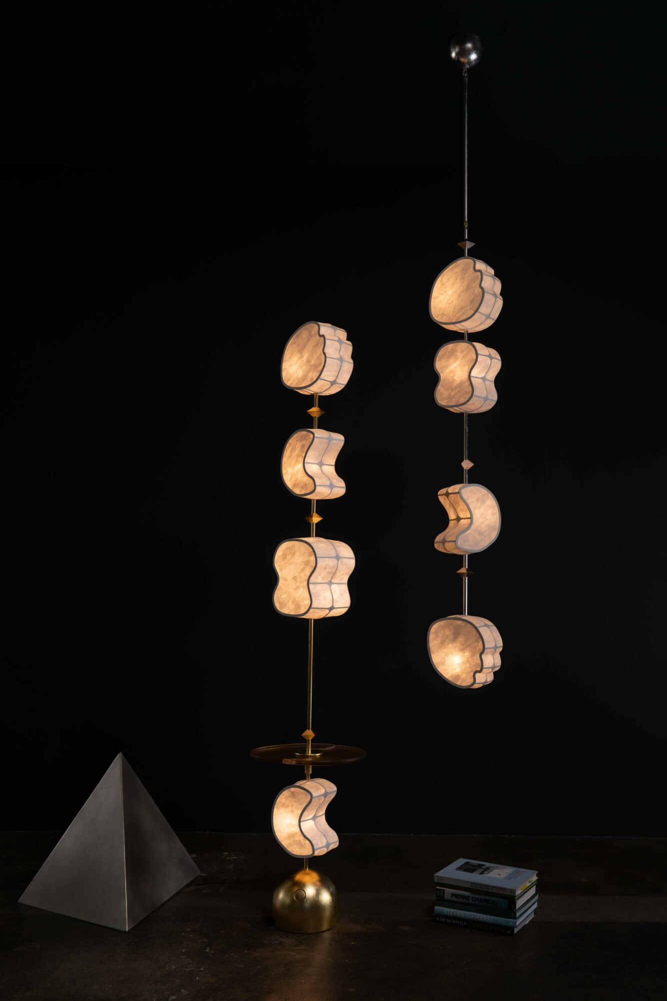 Two hanging lamps with wooden and metal elements, one with a pyramid shape and the other with a spherical base, against a black background.