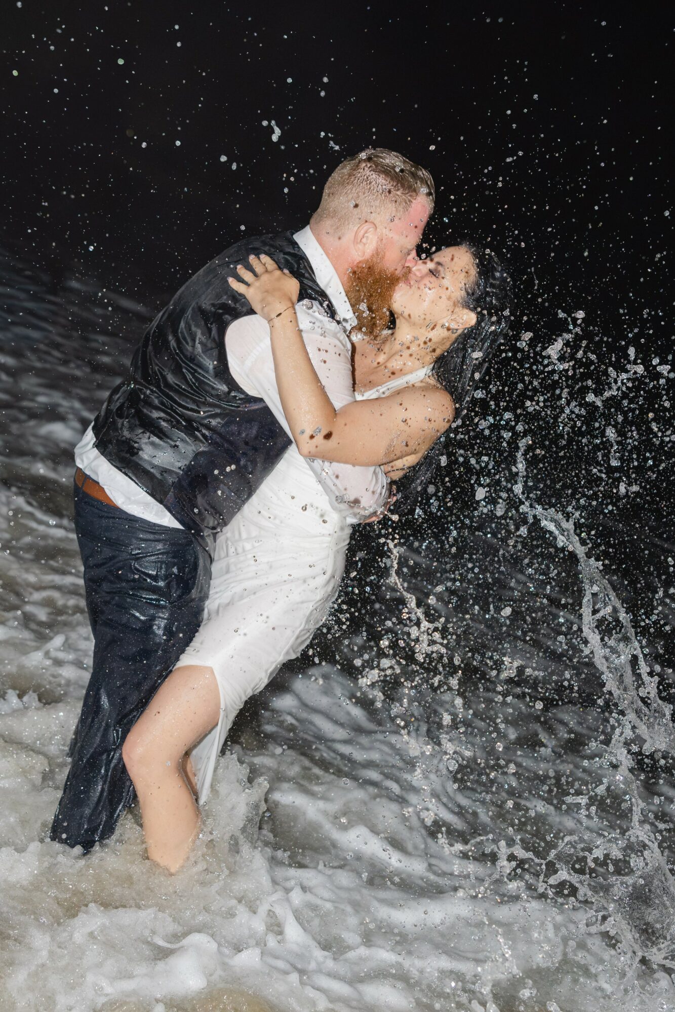 A couple kissing in water with splashes, at night, with stars visible in the sky.