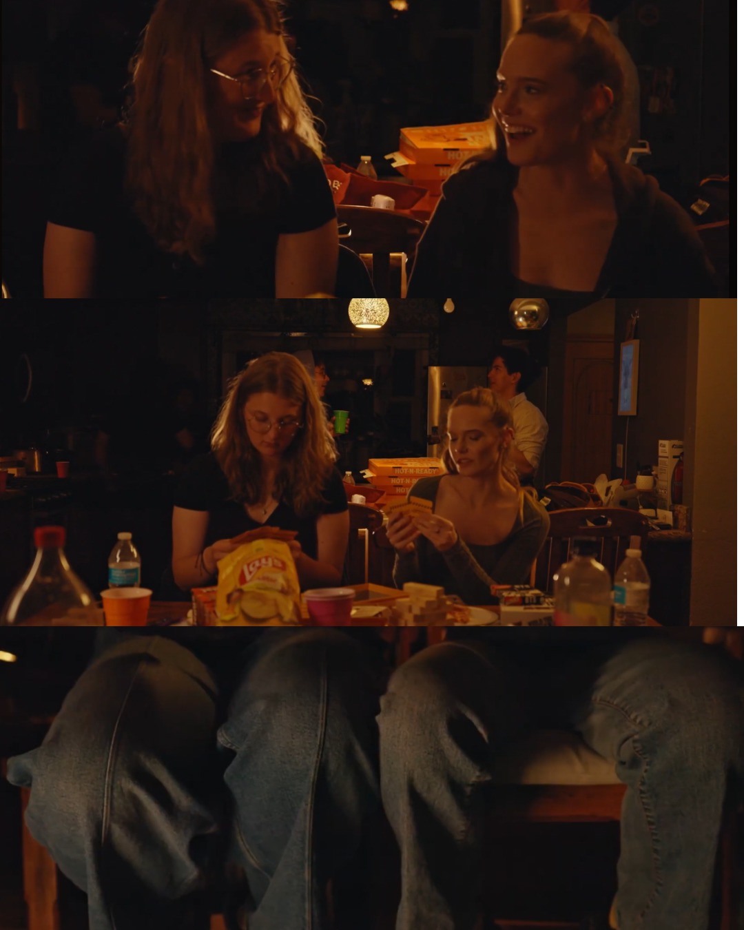 Two women sitting at a table in a dimly lit setting, smiling and talking, with snacks and drinks on the table.