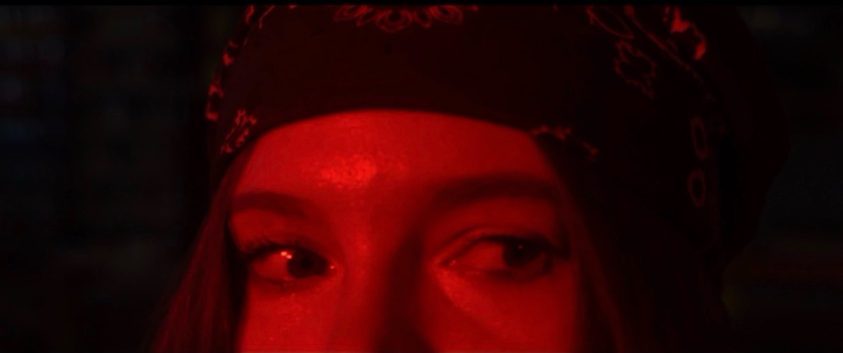 Close-up of a person's eyes and forehead with red lighting, wearing a patterned head covering.