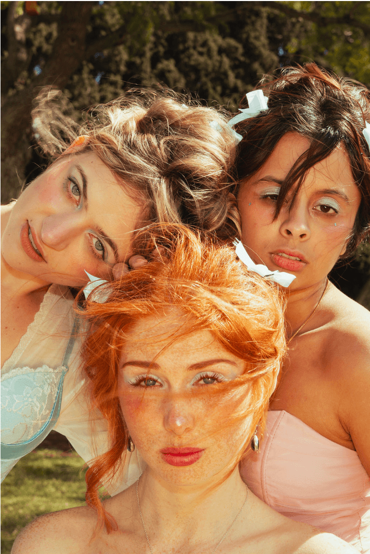 Three women with different hair colors and styles outdoors, close together, looking at the camera.