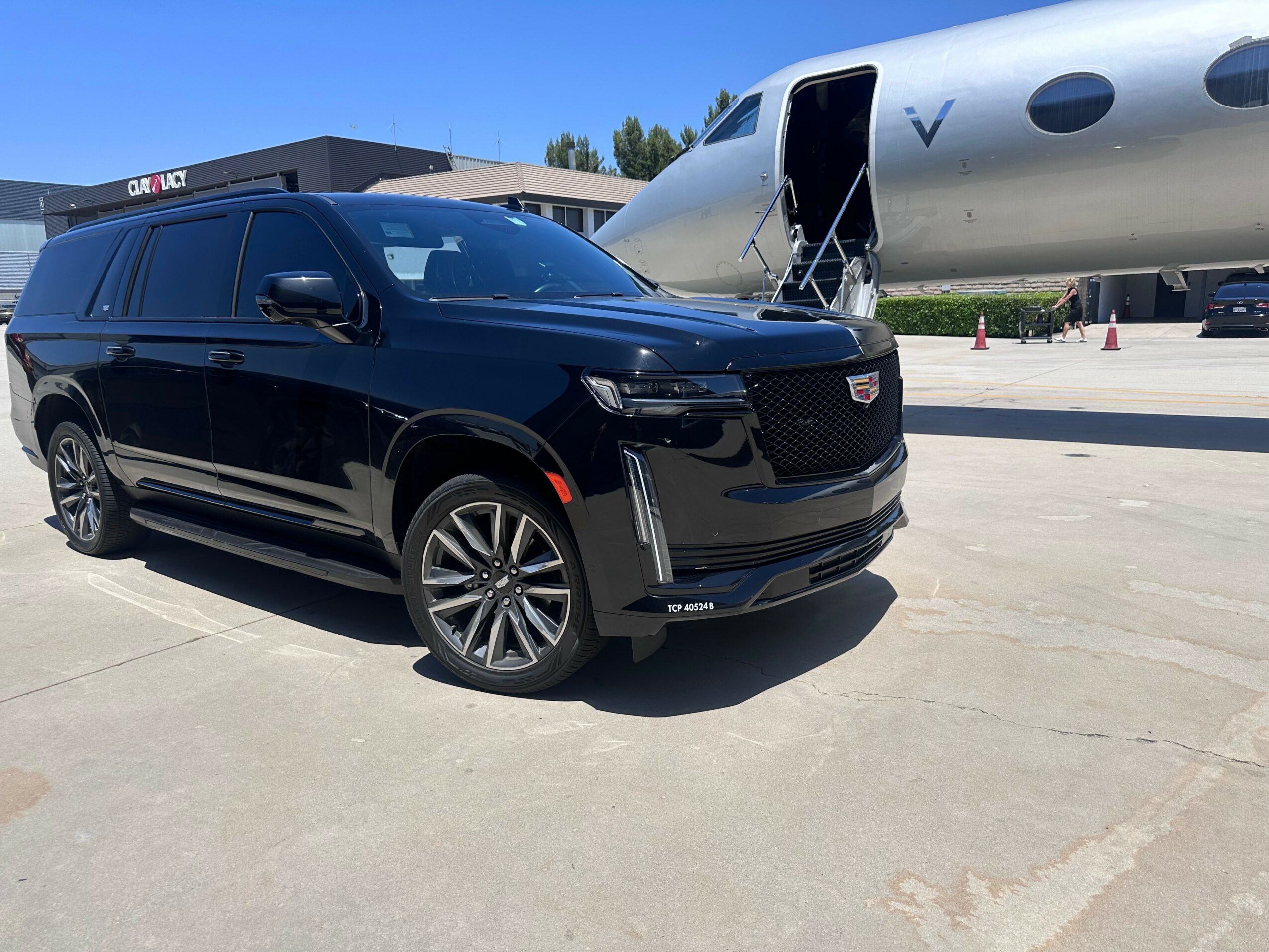 Black SUV parked near a private jet on tarmac, with airport buildings in background.
