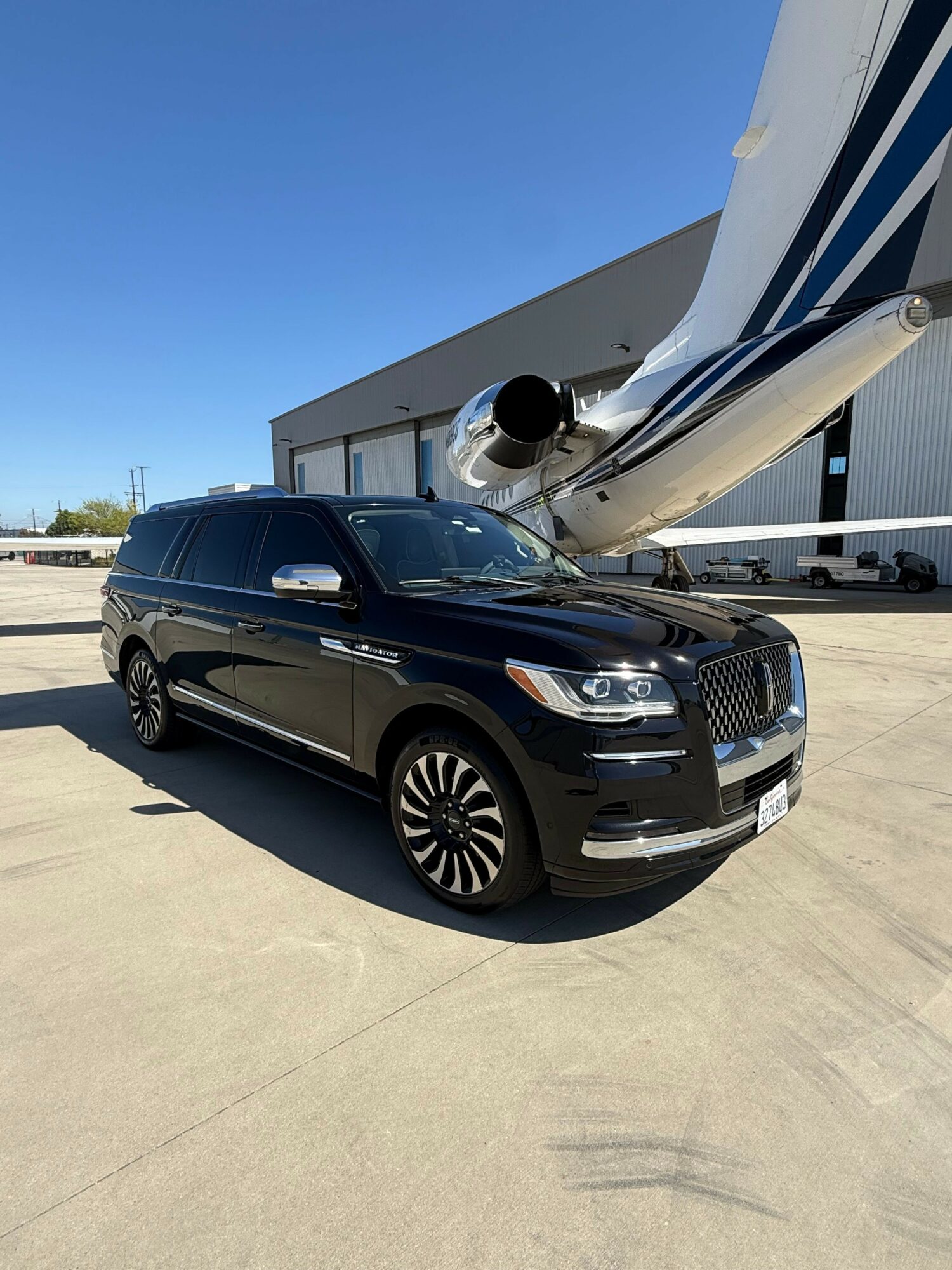 Black car parked on concrete surface with a building and blue sky in background.
