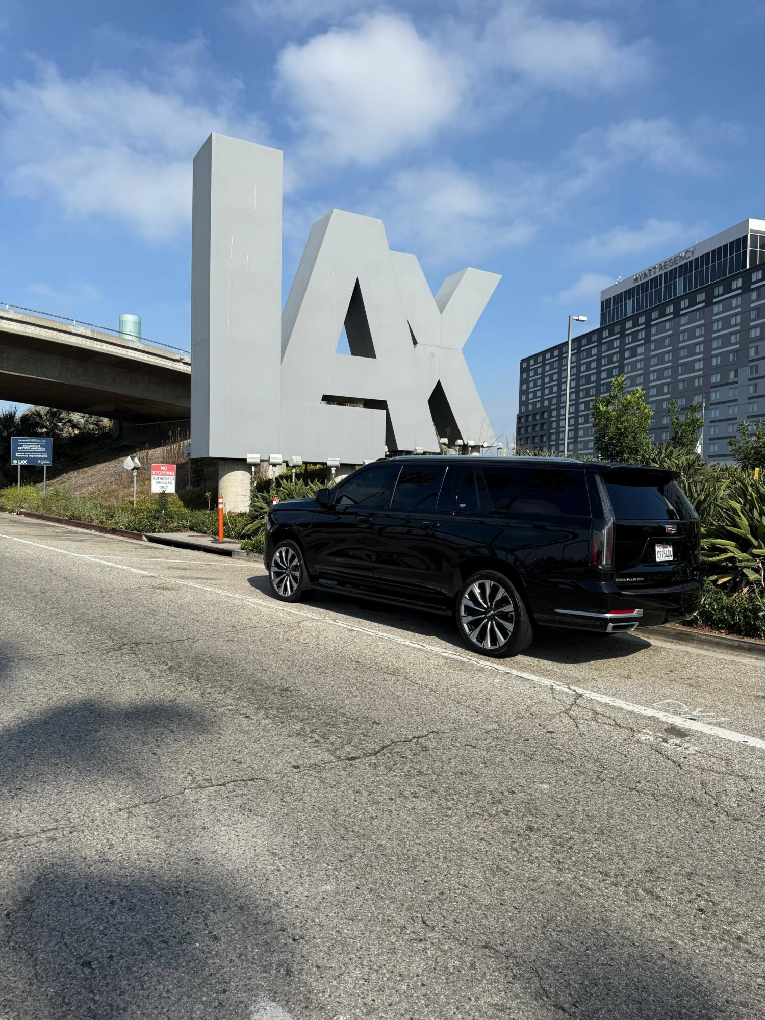 Black vehicle parked on the side of a road with a large LA sign and modern buildings in the background.