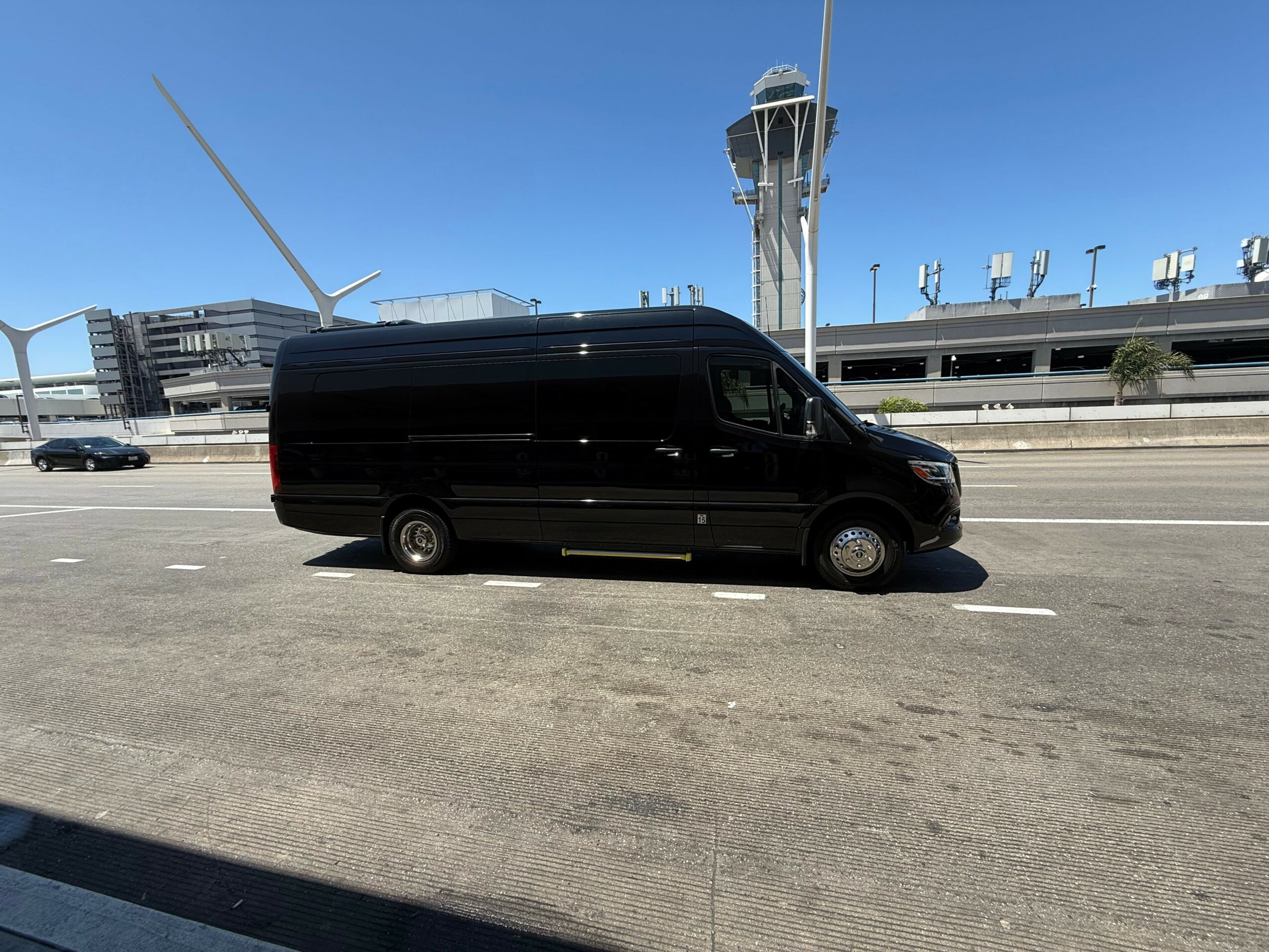 Black van parked on a wide road with airport structures and a control tower in the background.