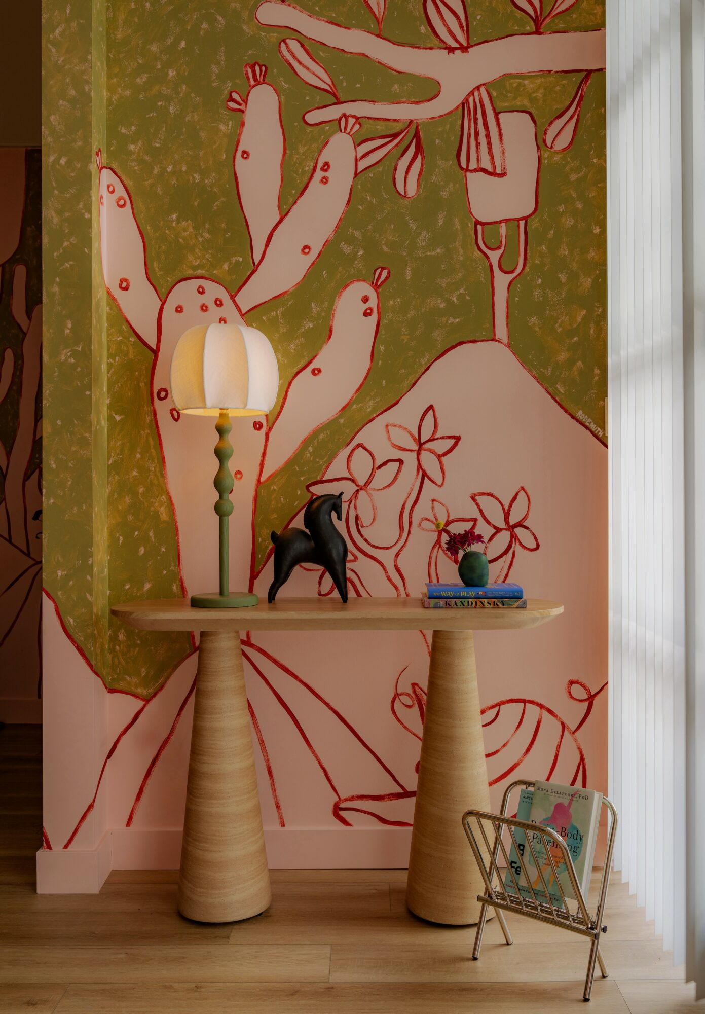 Decorative table with a lamp, a black shoe, a small plant, and books, against a colorful wall with abstract art.