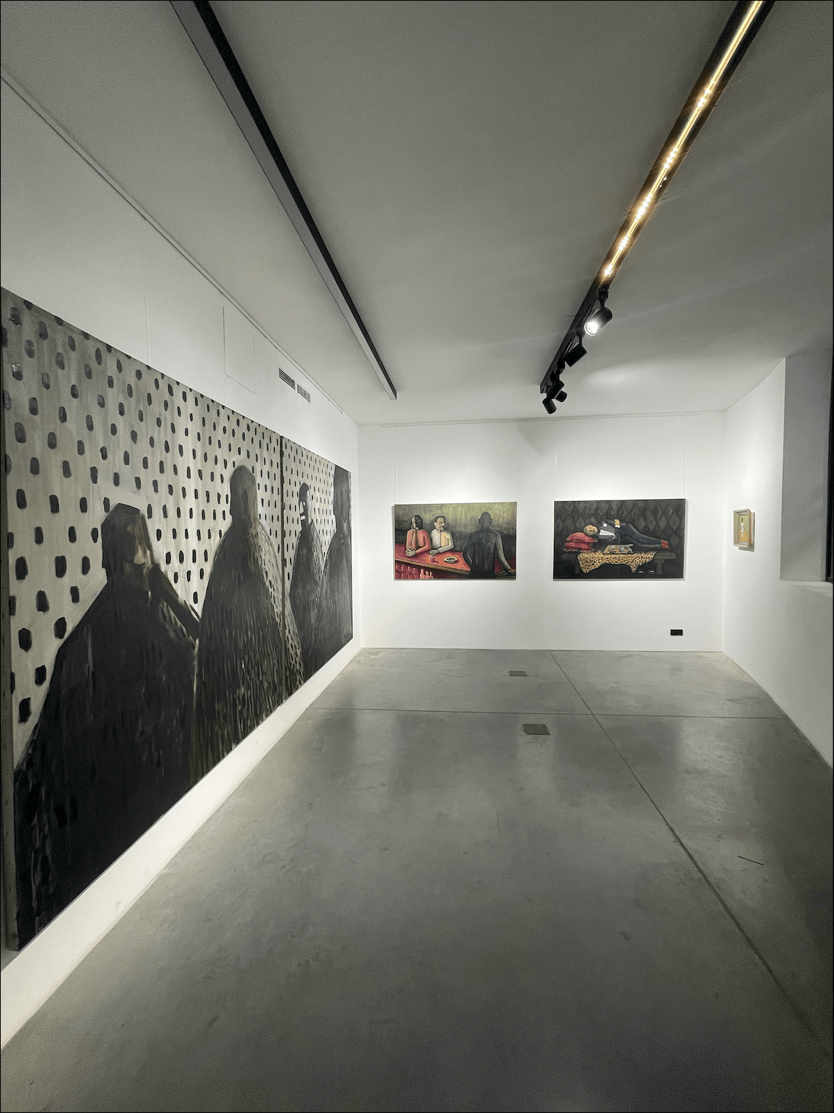 Gallery with large black and white artwork on the left wall and two colorful paintings on the back wall, minimal lighting.