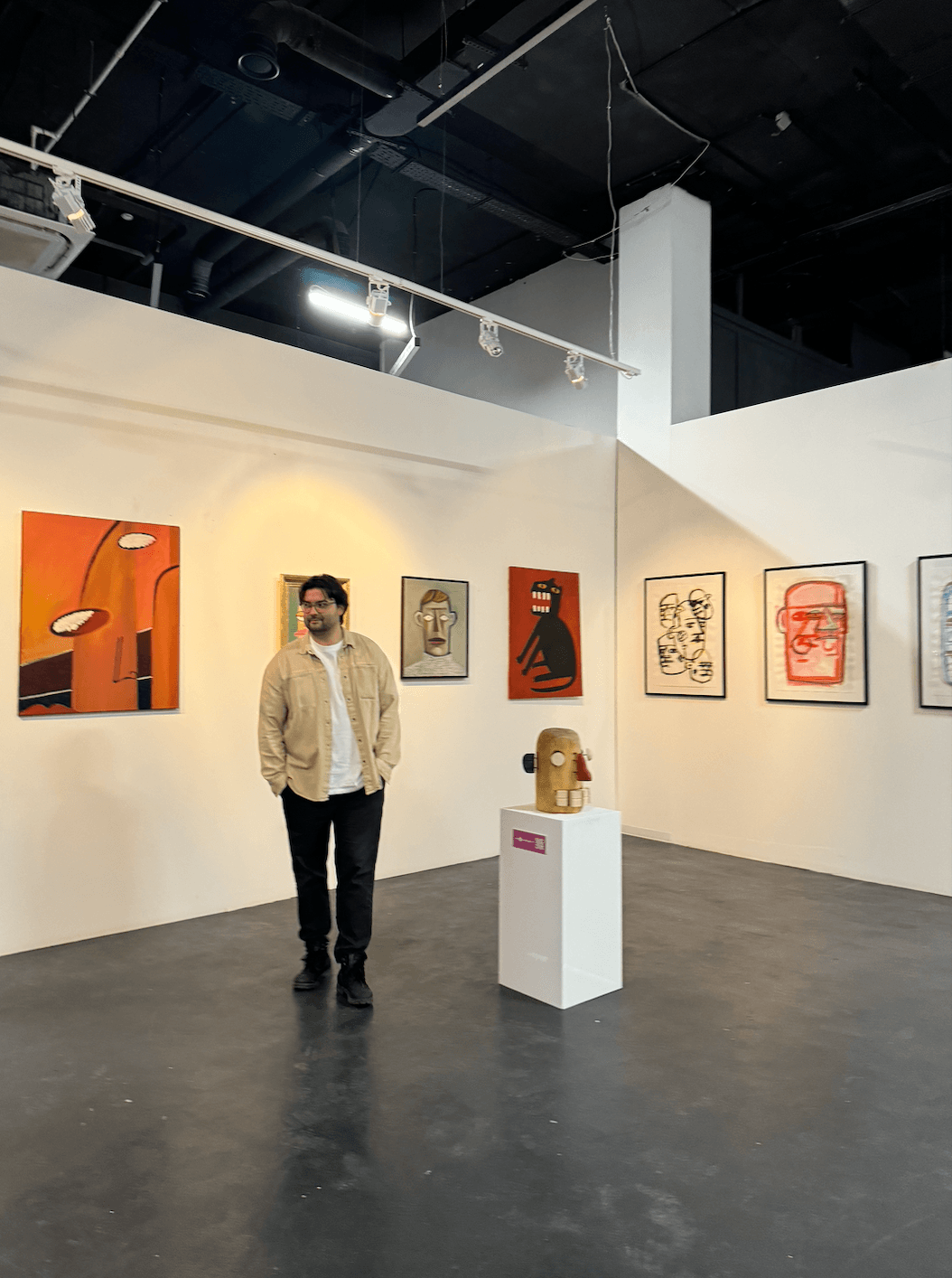 Person standing in an art gallery with colorful paintings on white walls and a sculpture on a pedestal.