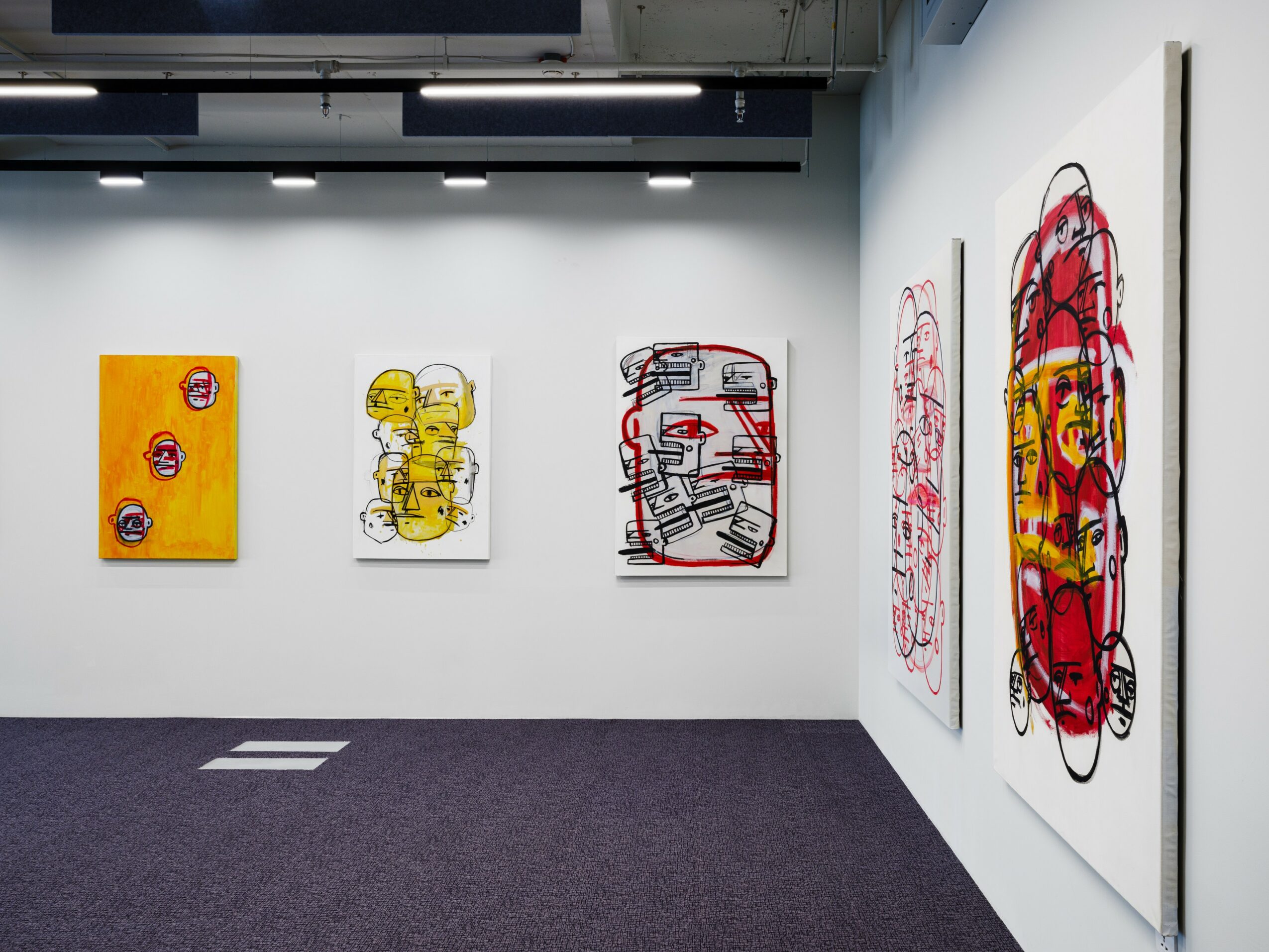 Gallery wall with five abstract colorful paintings, white walls, dark carpeted floor, and ceiling lights.