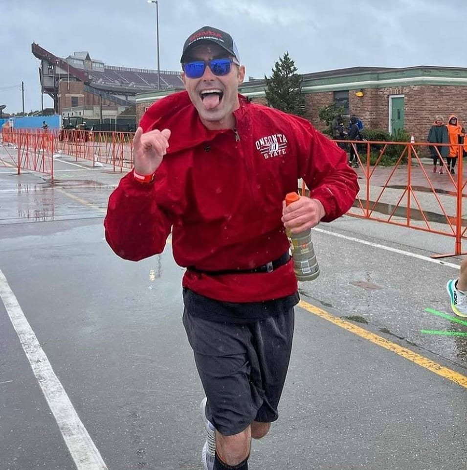 Person smiling and celebrating outdoors on a rainy day, wearing sunglasses, a red jacket, and holding a water bottle.