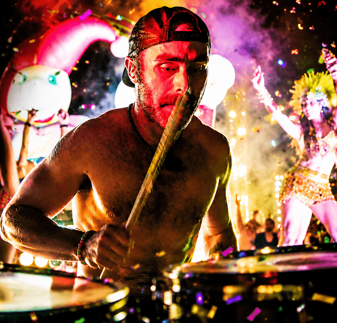 Male DJ wearing a cap, focused on mixing music at a lively outdoor event with colorful lights and decorations.