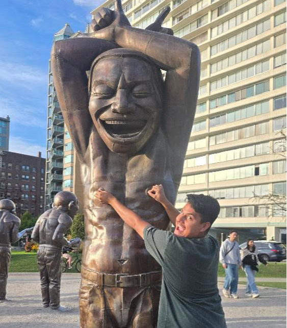 Young man punching a large smiling statue in an urban park with buildings and people in the background.