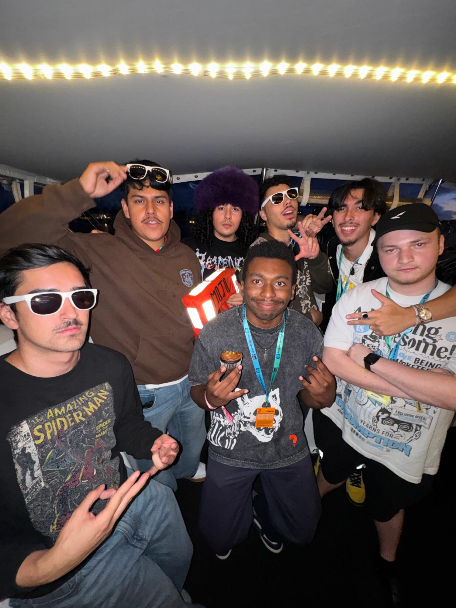 Group of people posing together, some making peace signs, in a dimly lit setting with a bright strip of light above.