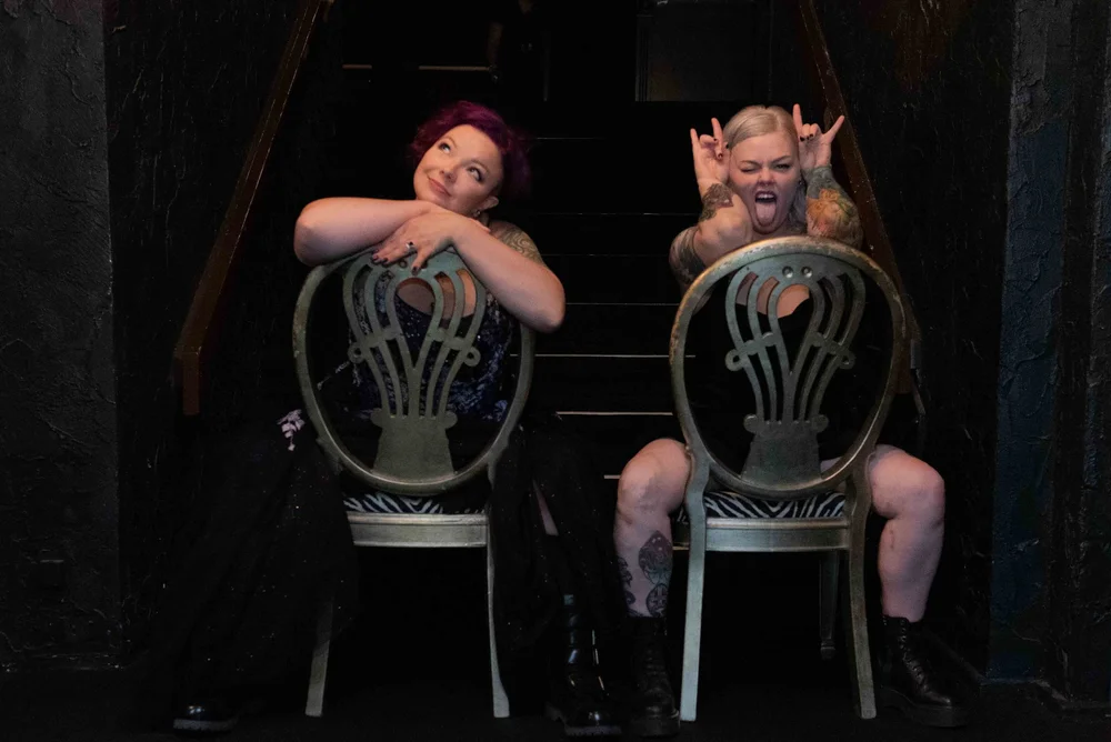 Two people sitting on chairs on a staircase, making playful gestures and expressions.