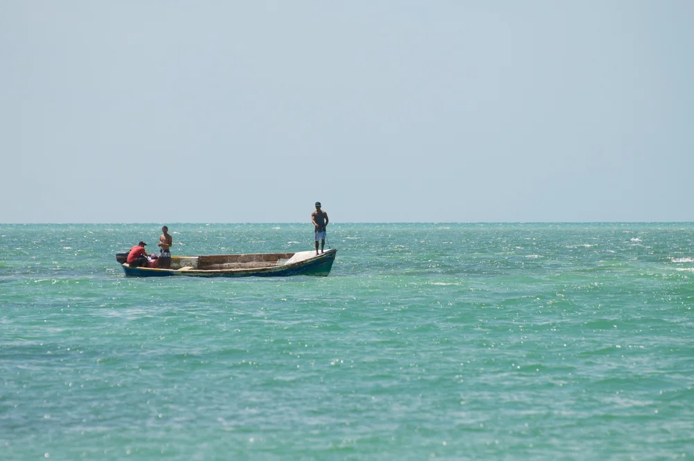 Three people on a boat floating on calm ocean water with a clear sky background.