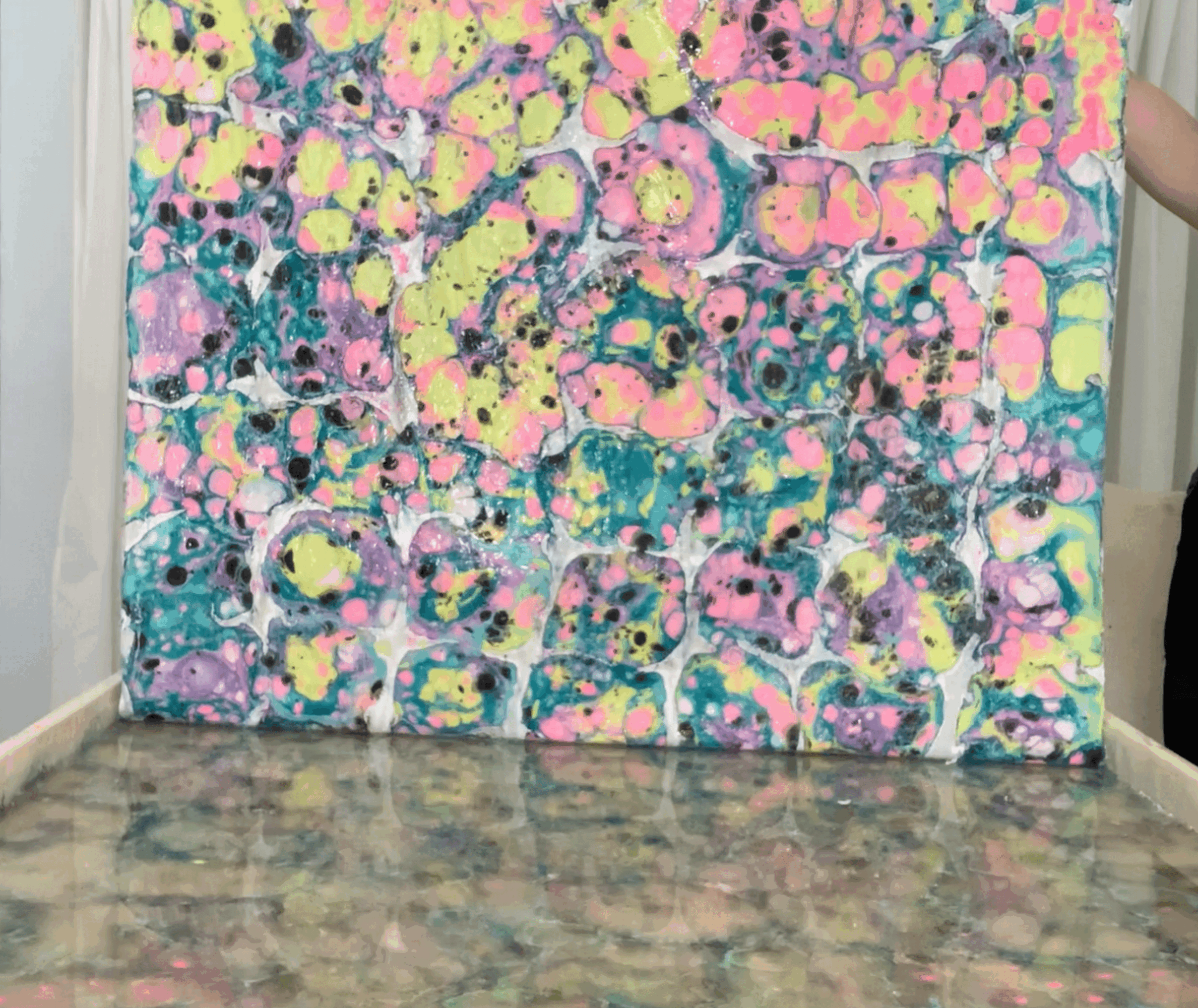 Colorful abstract painting with pink, yellow, blue, and green splashes on a canvas, placed on a marble surface.