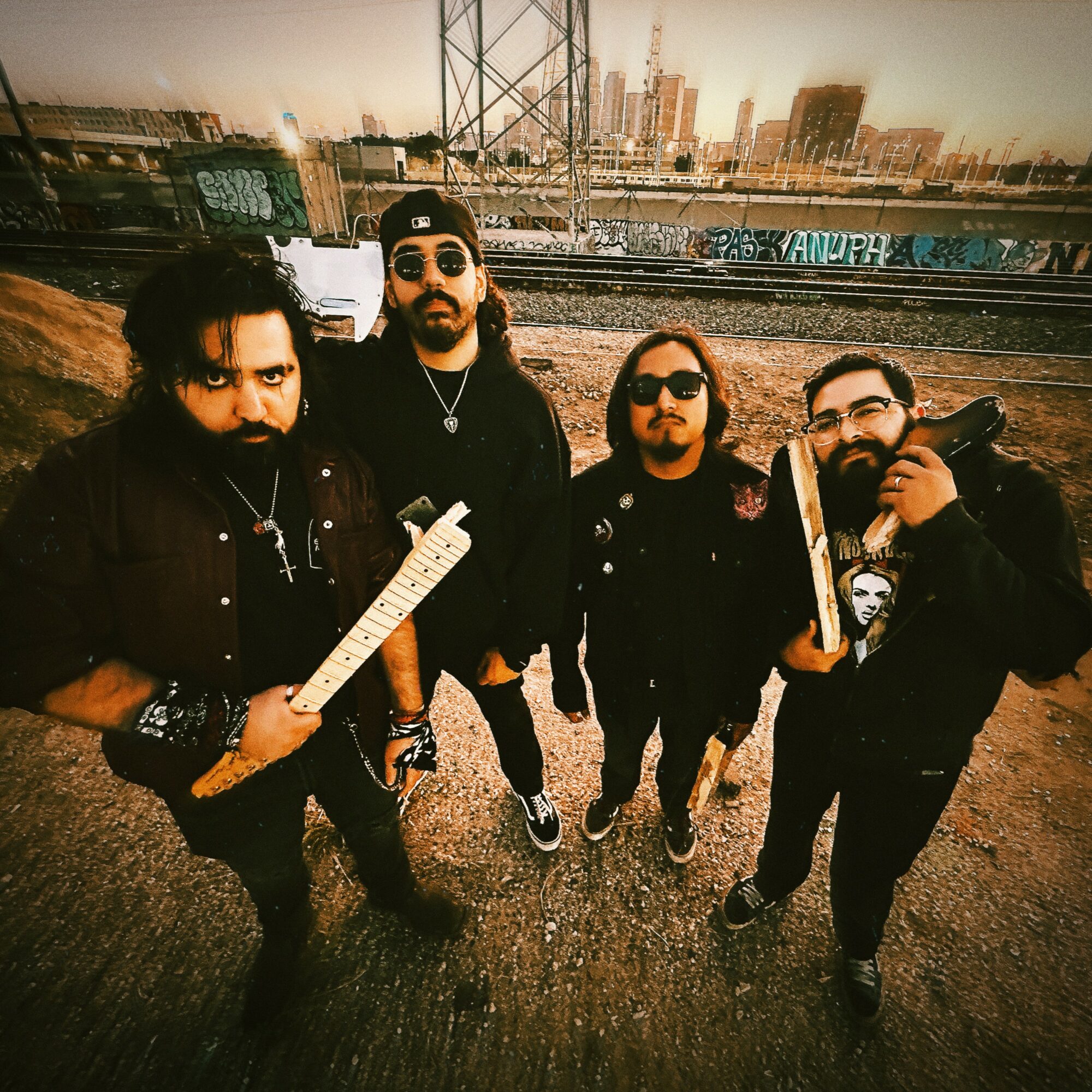 Four men standing outdoors near train tracks with a city skyline in the background, posing for a photo.