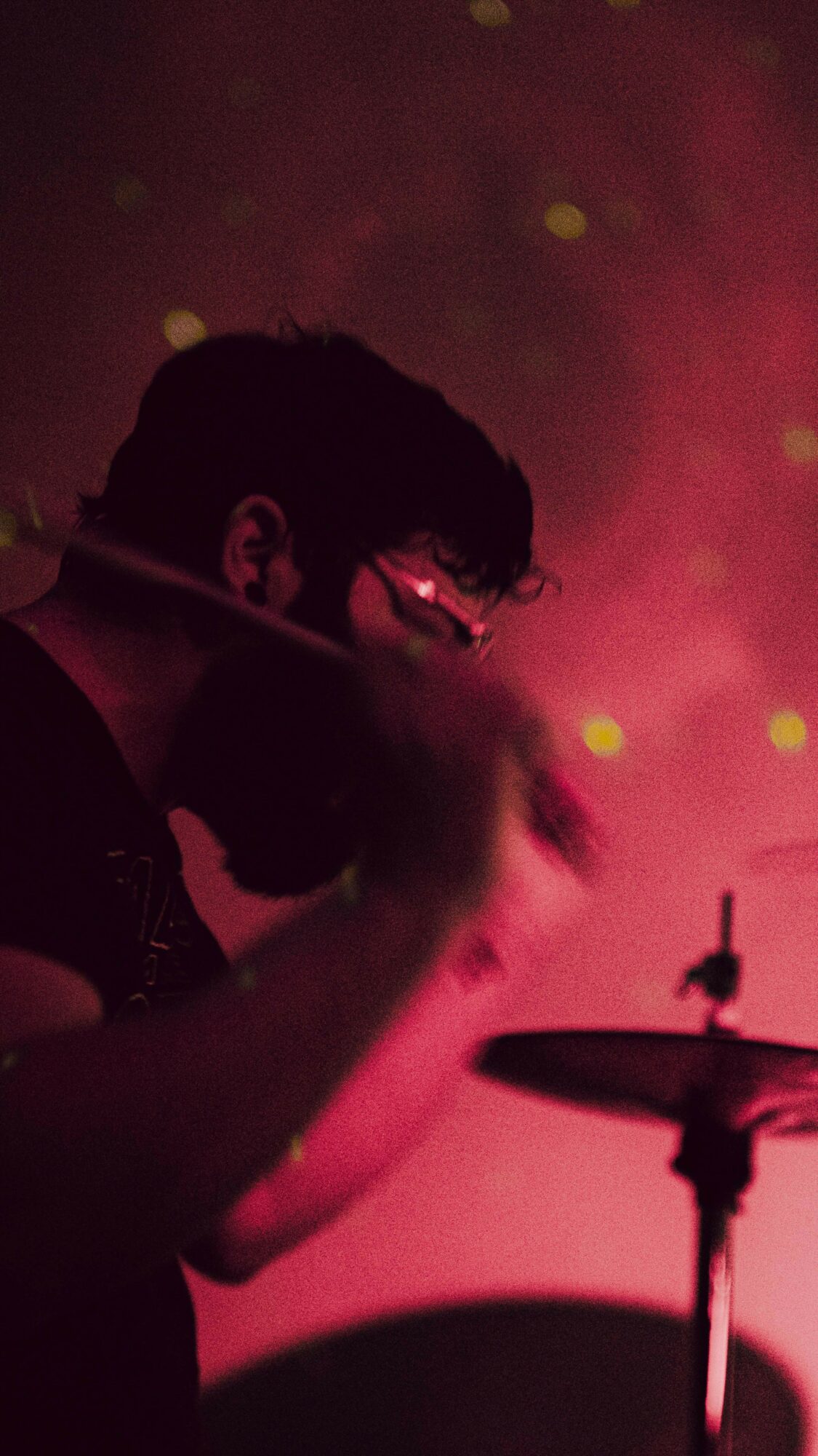 Silhouette of a person playing drums with a pink and yellow background.