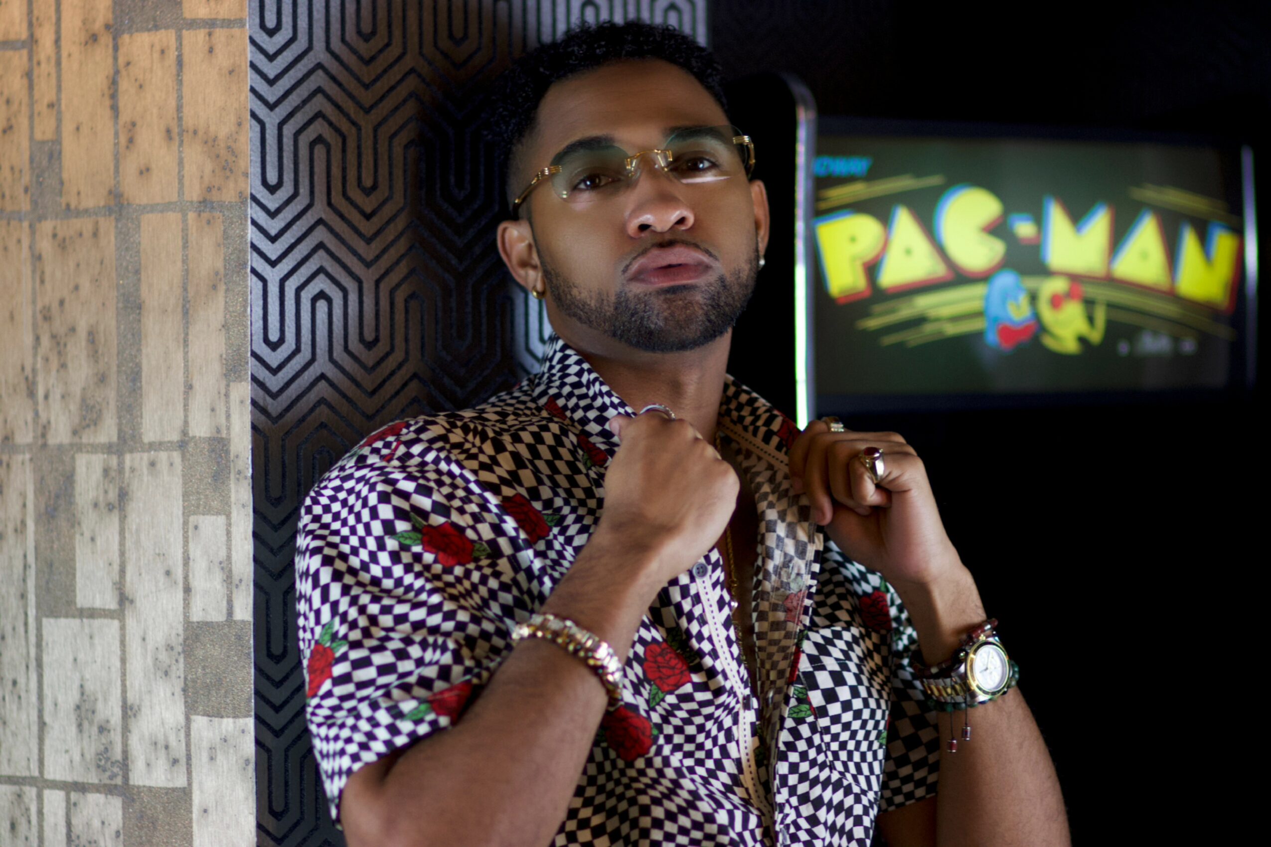 Man with glasses and beard wearing a patterned shirt, standing indoors with a Pac-Man sign in the background.