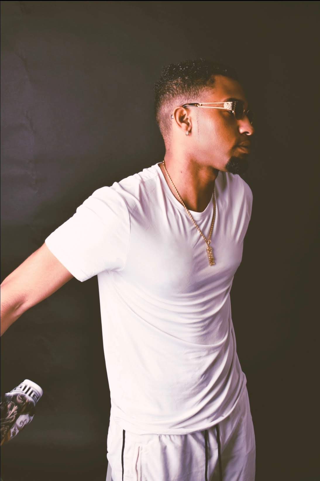 Young man in white t-shirt and sunglasses, facing right, against a dark background.