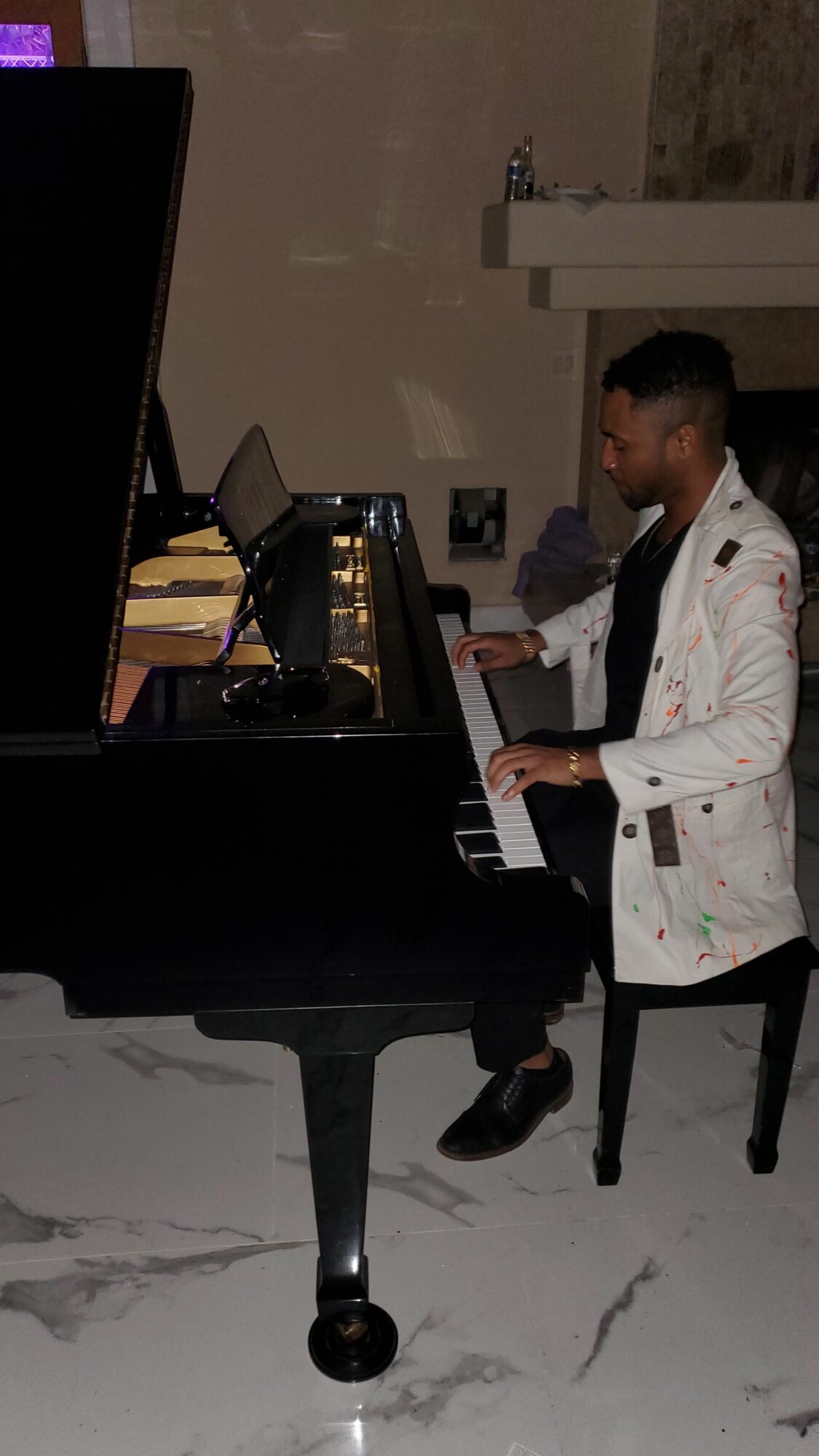 Person in a white coat standing next to a black grand piano in a room with marble flooring.