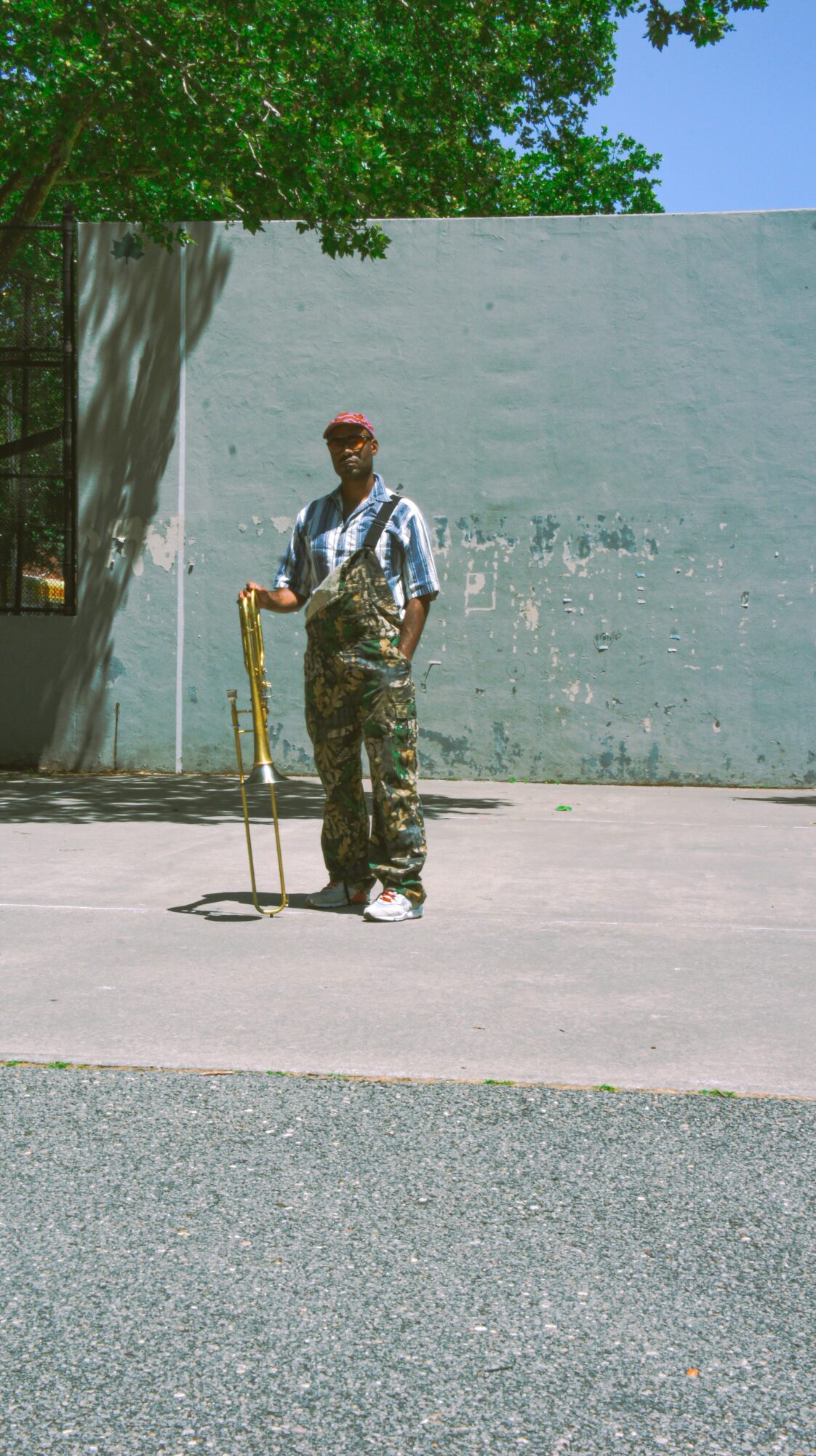 Person standing outdoors holding a yellow measuring tape, with a large light blue wall and green tree in background.