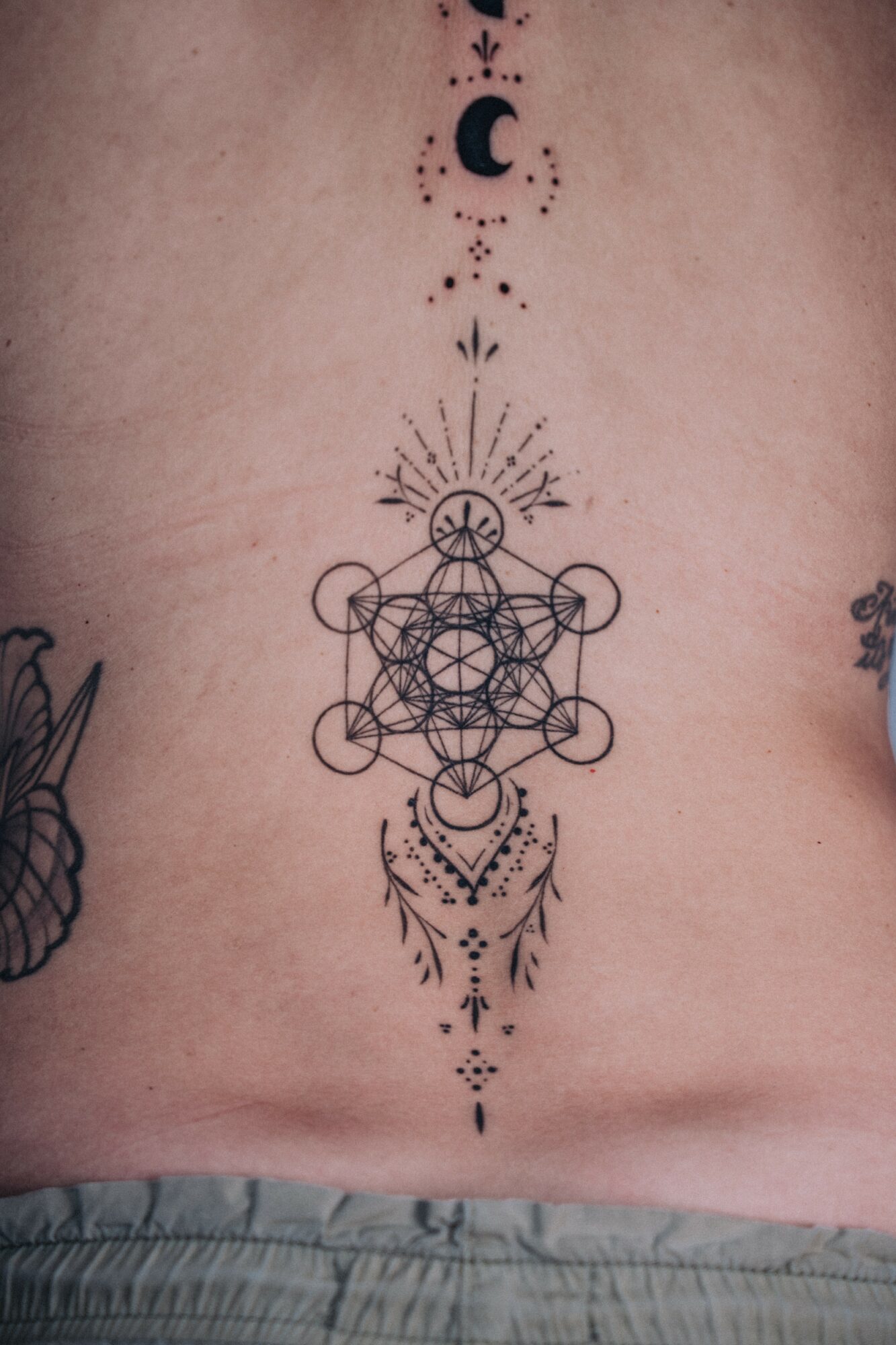 Vertical tattoo with geometric patterns, celestial symbols, and decorative elements on a person's chest.