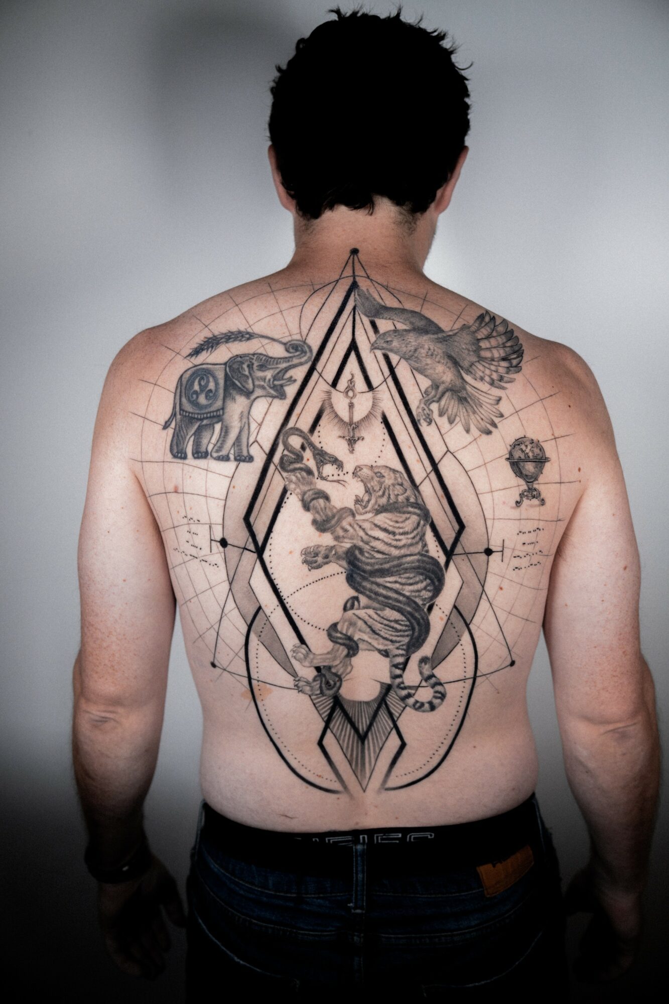 Back of a person with tattoos, including a large geometric design and various images, facing away from the camera.