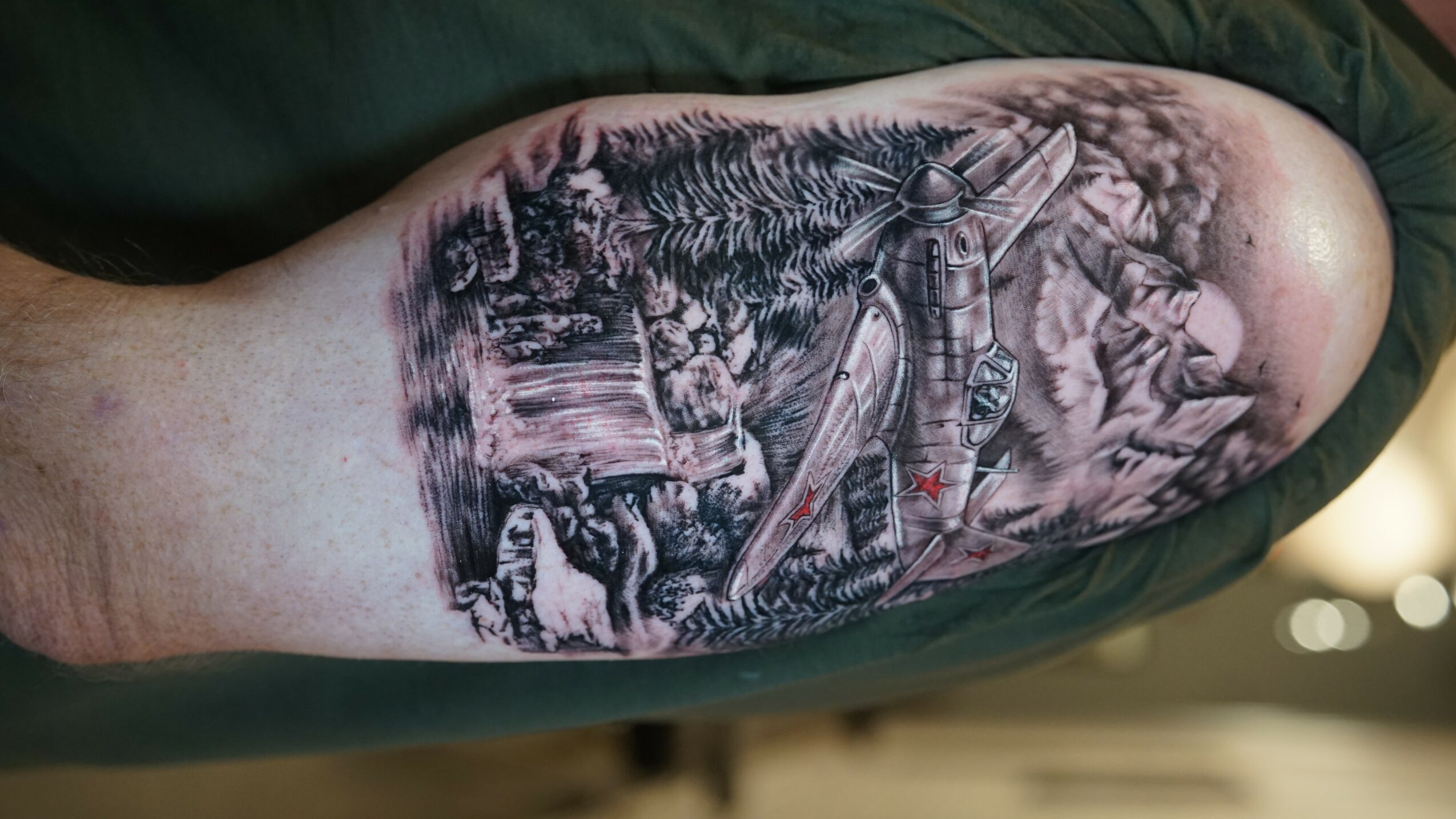 Tattoo of a forest scene with trees, a river, and a person fishing with a fishing rod, in black and gray ink.