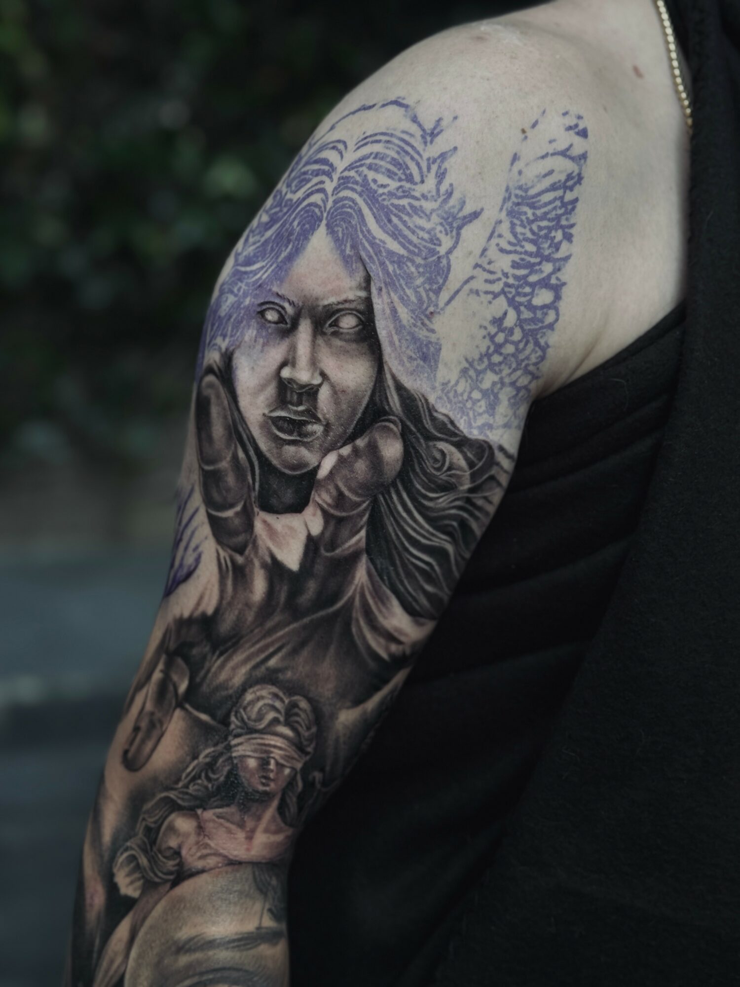 Tattoo of a woman's face with flowing hair, reaching out with her hand, on a person's upper arm.