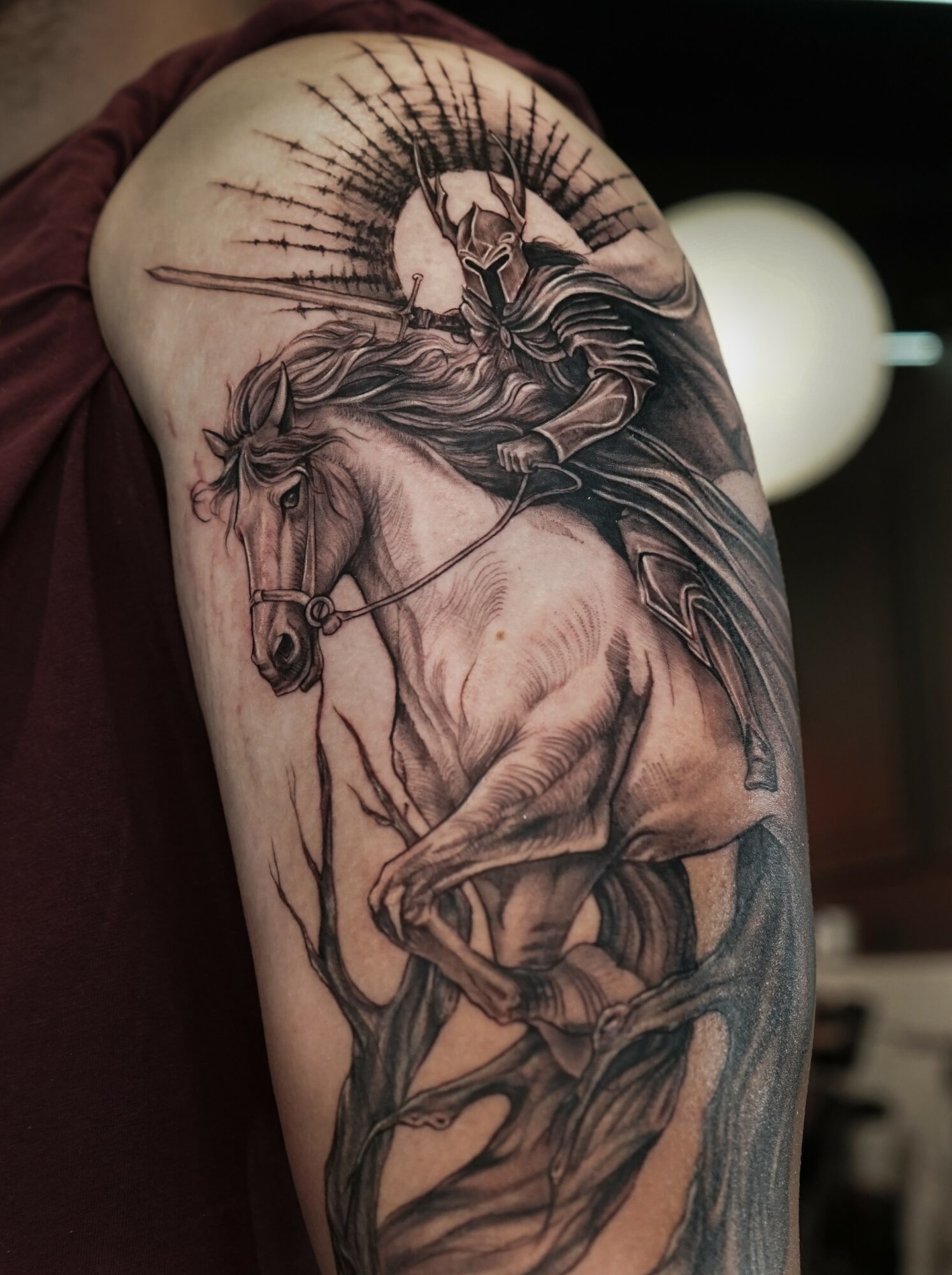 Detailed black and gray tattoo of a horse with a rider, surrounded by a halo and abstract elements.