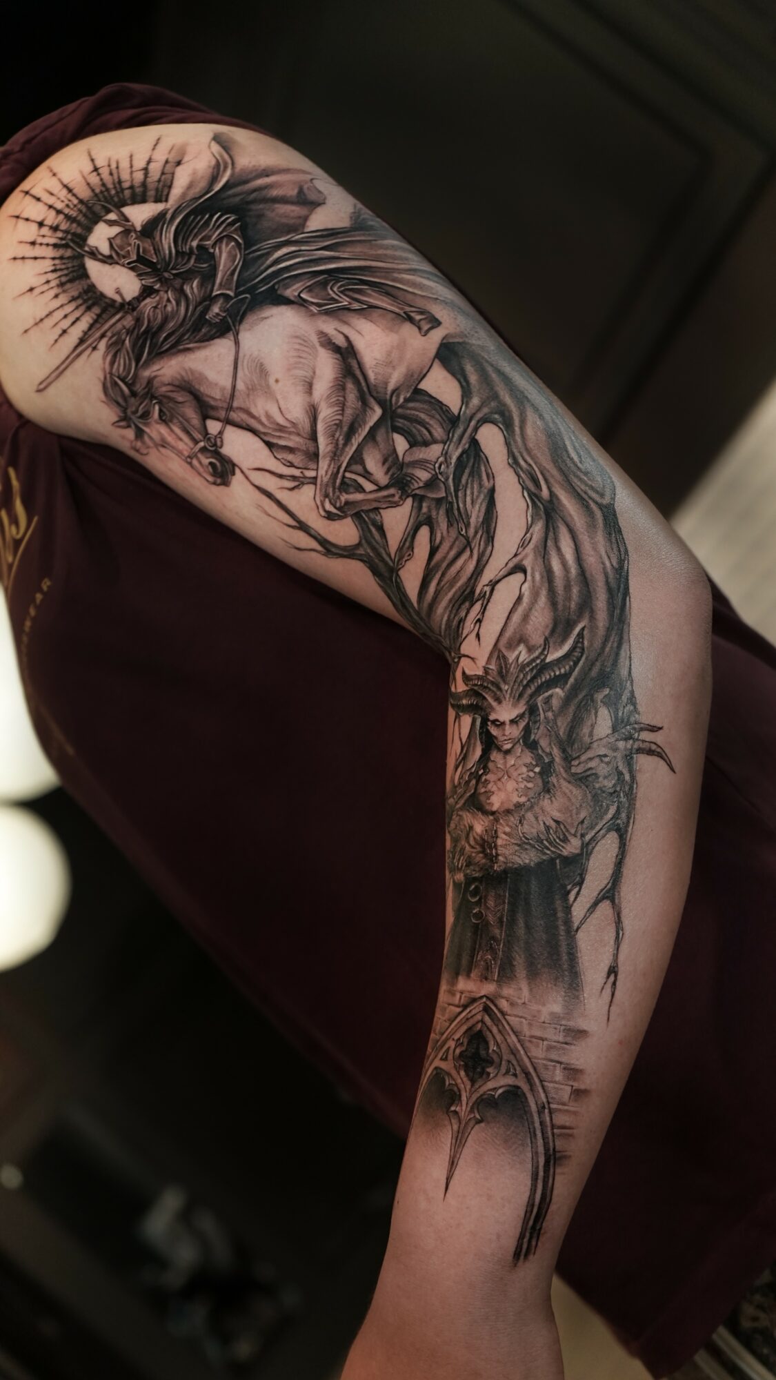 Tattoo of a horse with a rider, surrounded by trees and a moon, on a person's arm.