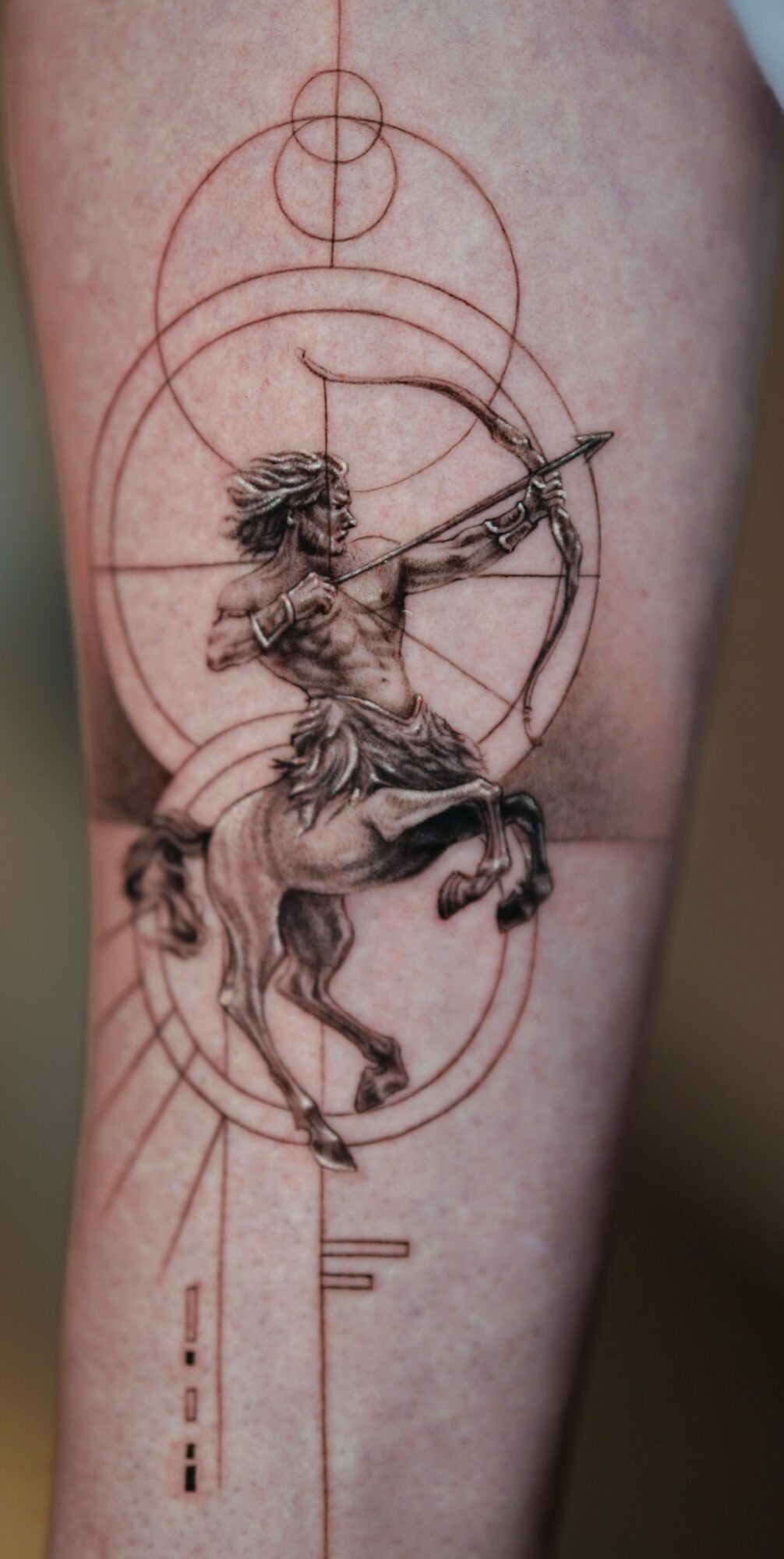 Tattoo of a person riding a horse, aiming a bow, with geometric circles and lines in the background.