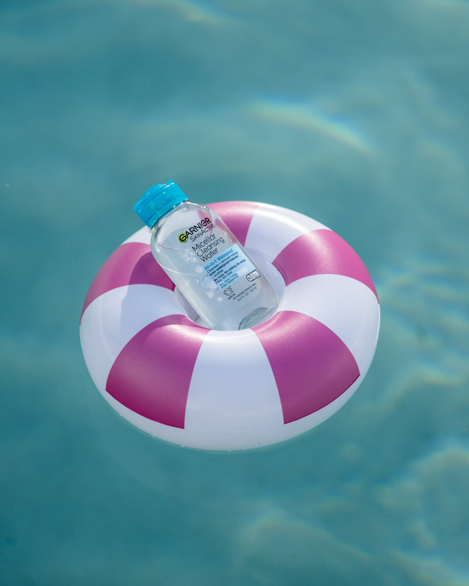 A plastic water bottle resting on a pink and white striped inflatable ring in a swimming pool.