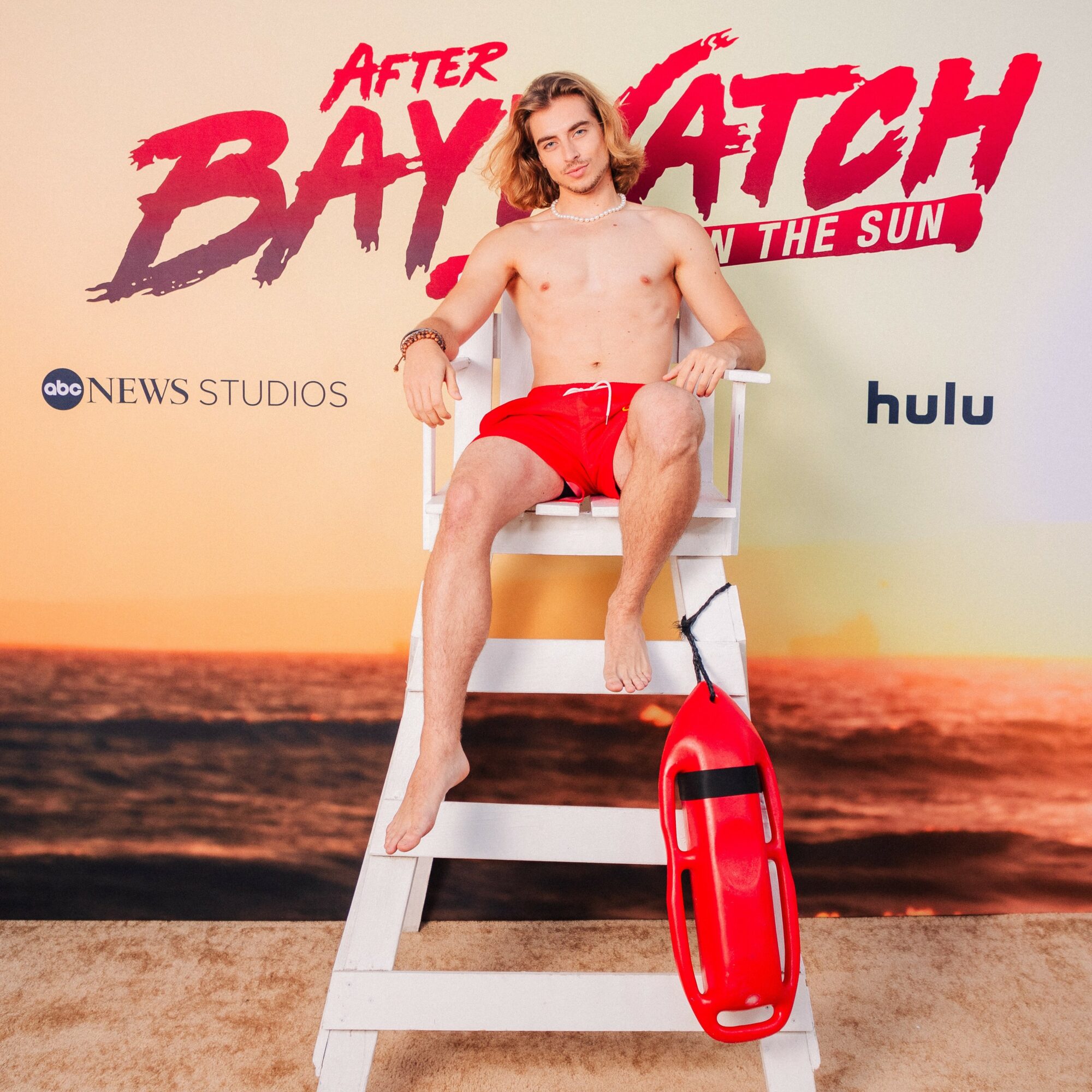 Person sitting on a lifeguard chair with a red rescue tube, beach background, promotional text, and logos.