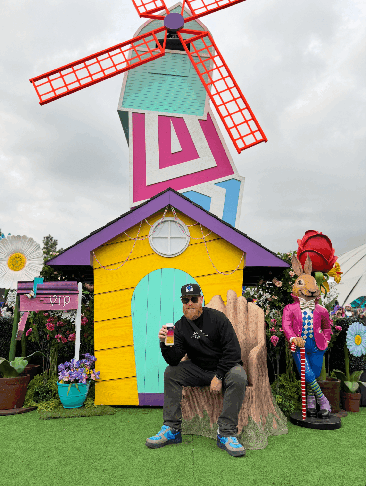 Person sitting on a tree stump in front of colorful house and windmill, with cartoon characters and flowers nearby.