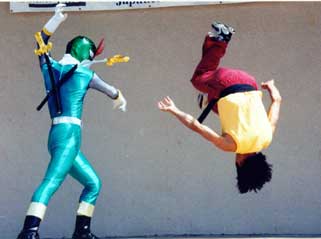 Person in a yellow vest flips upside down while another person in a blue costume appears to be hitting them with a stick.