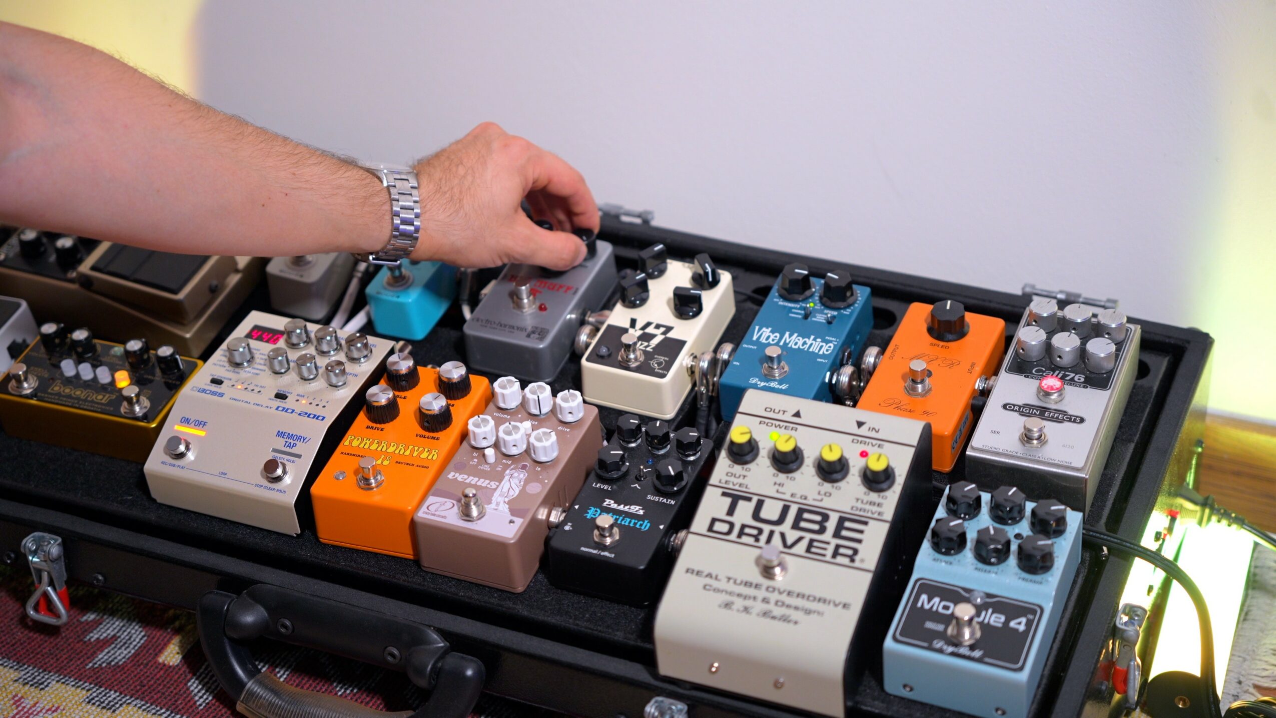 Person's hand adjusting guitar effects pedalboard with various colorful pedals and controls, on a black case.