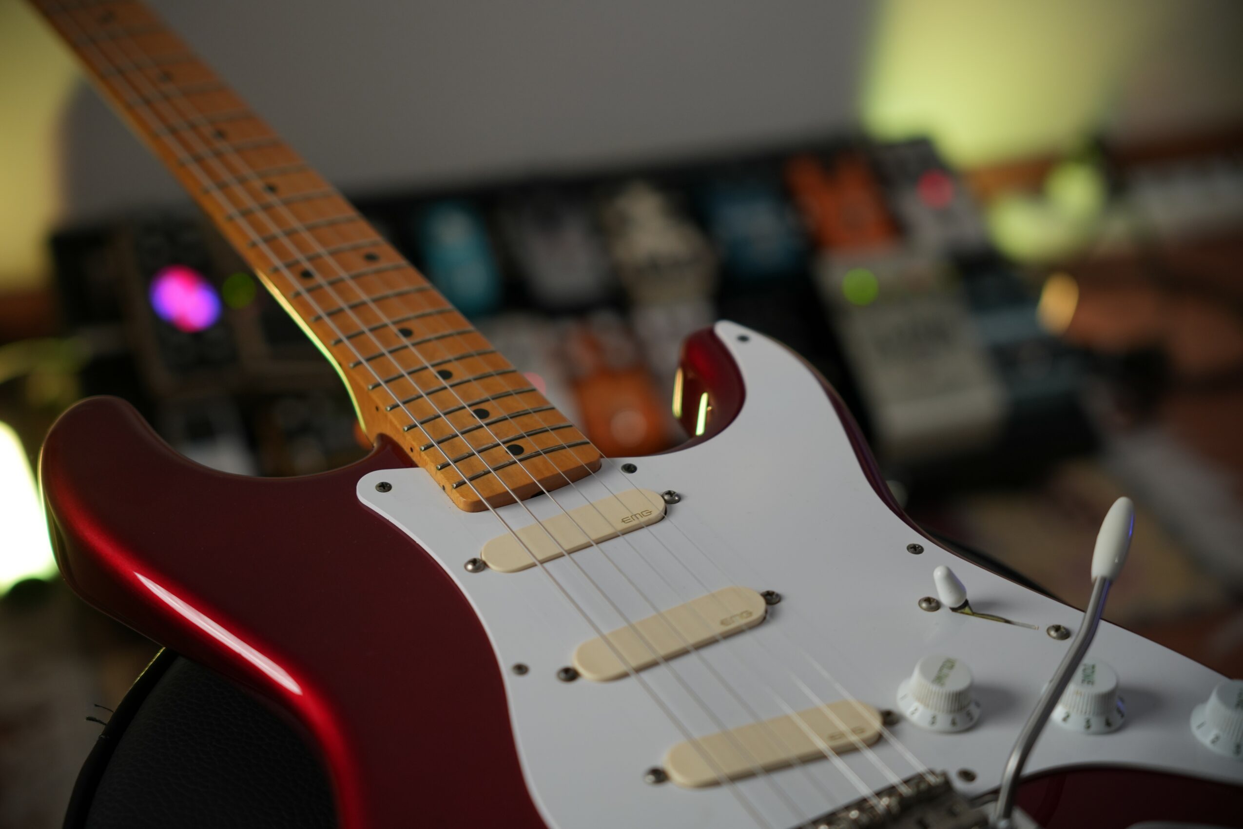 Electric guitar with a red body, white pickguard, and three pickups, in a music studio setting.