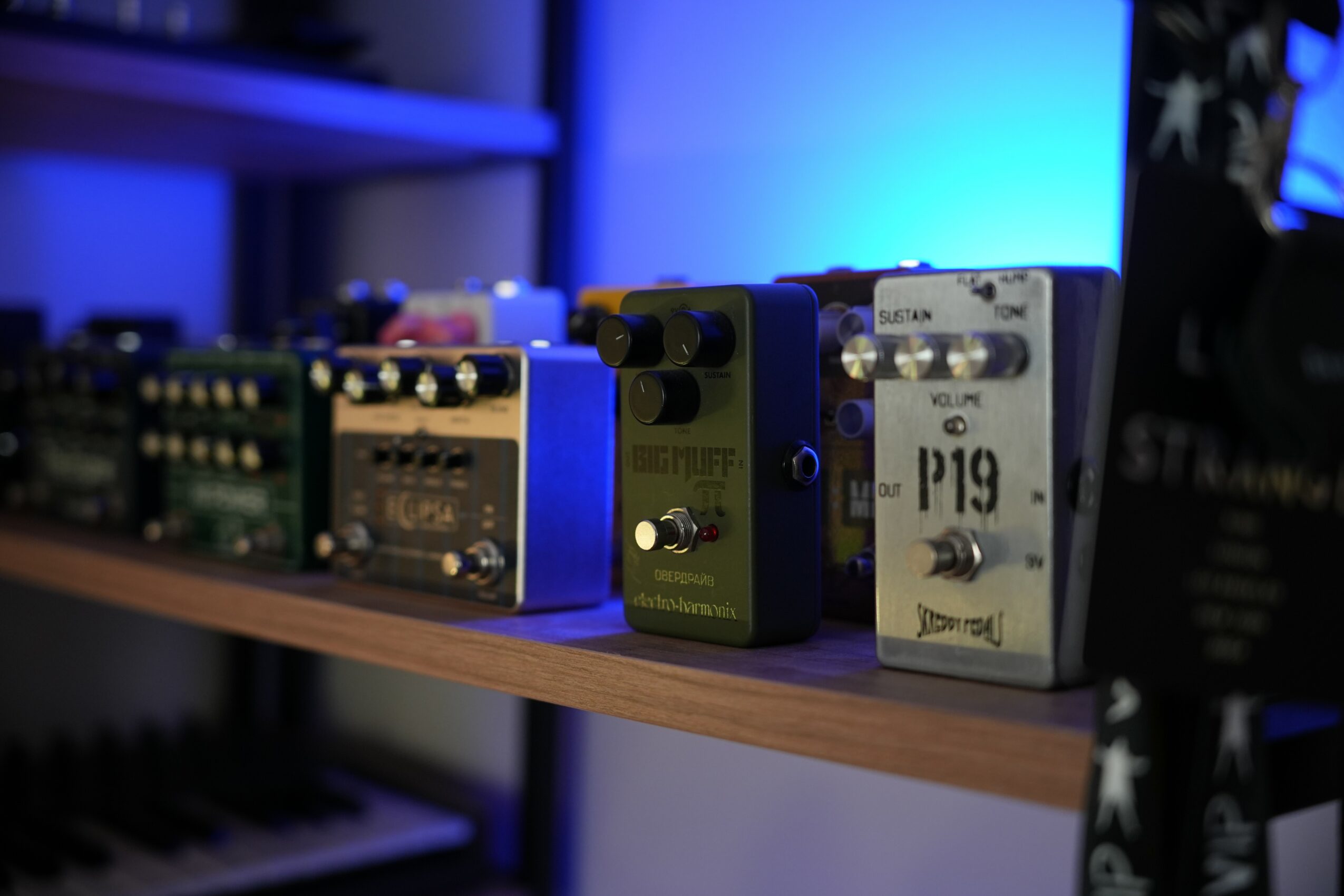 Row of guitar effect pedals on a wooden shelf, with blue lighting in the background.