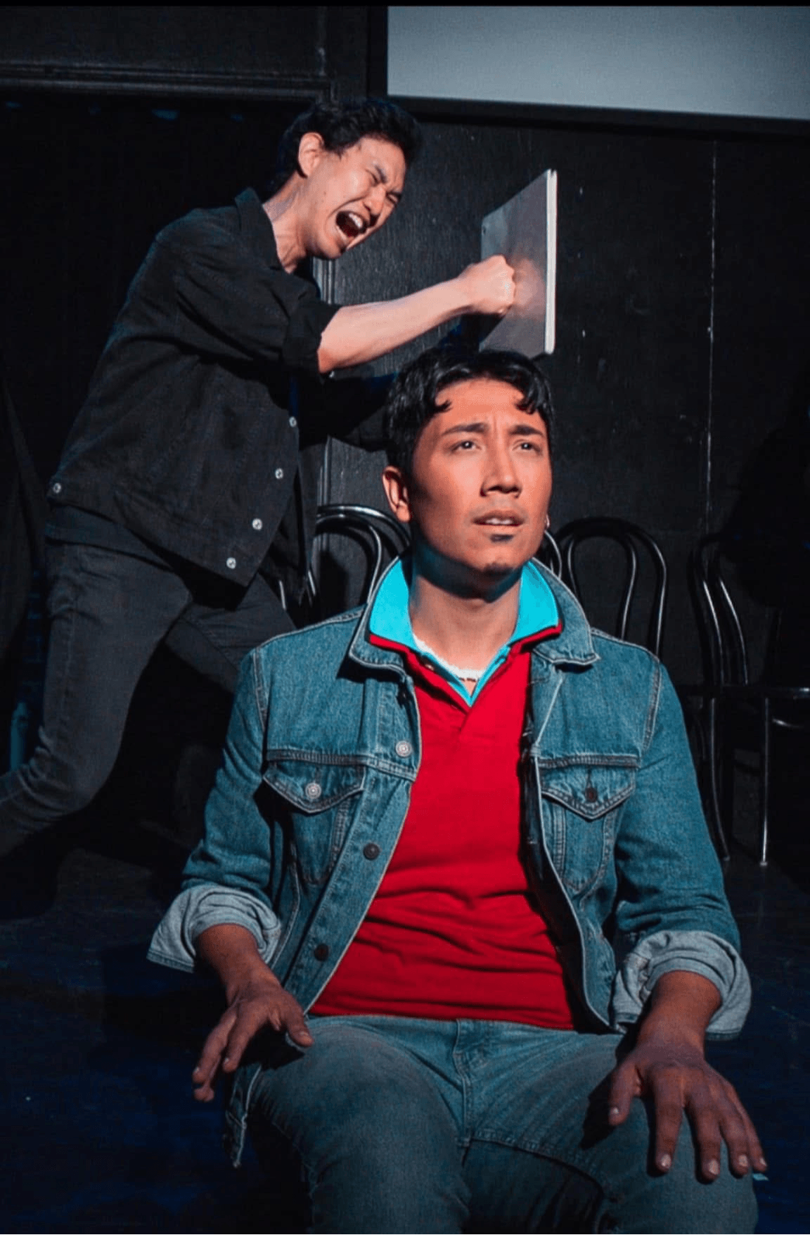 Woman appears to be hitting a man on the head with a book, man looks surprised or distressed, black background.
