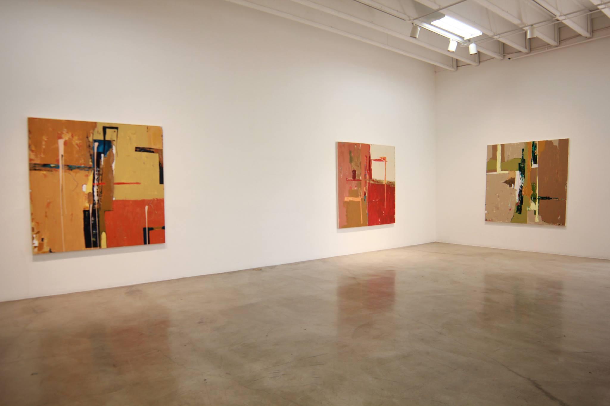 Three abstract paintings on a white gallery wall, with a polished concrete floor and ceiling lights, in an art gallery.