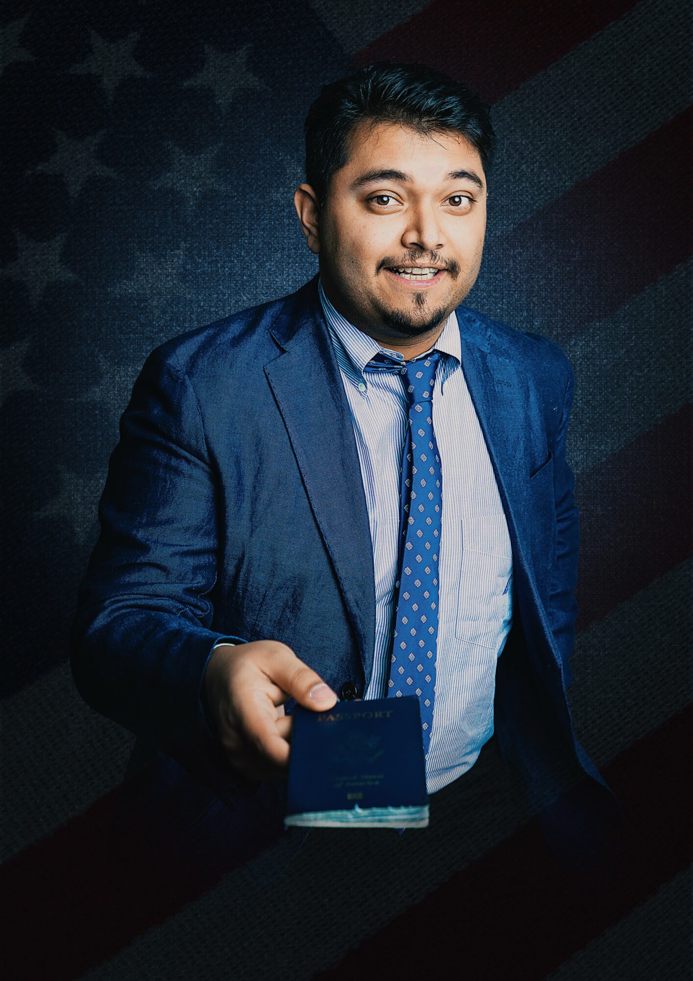 Man in a blue suit holding a smartphone, smiling, dark background with faint American flag pattern