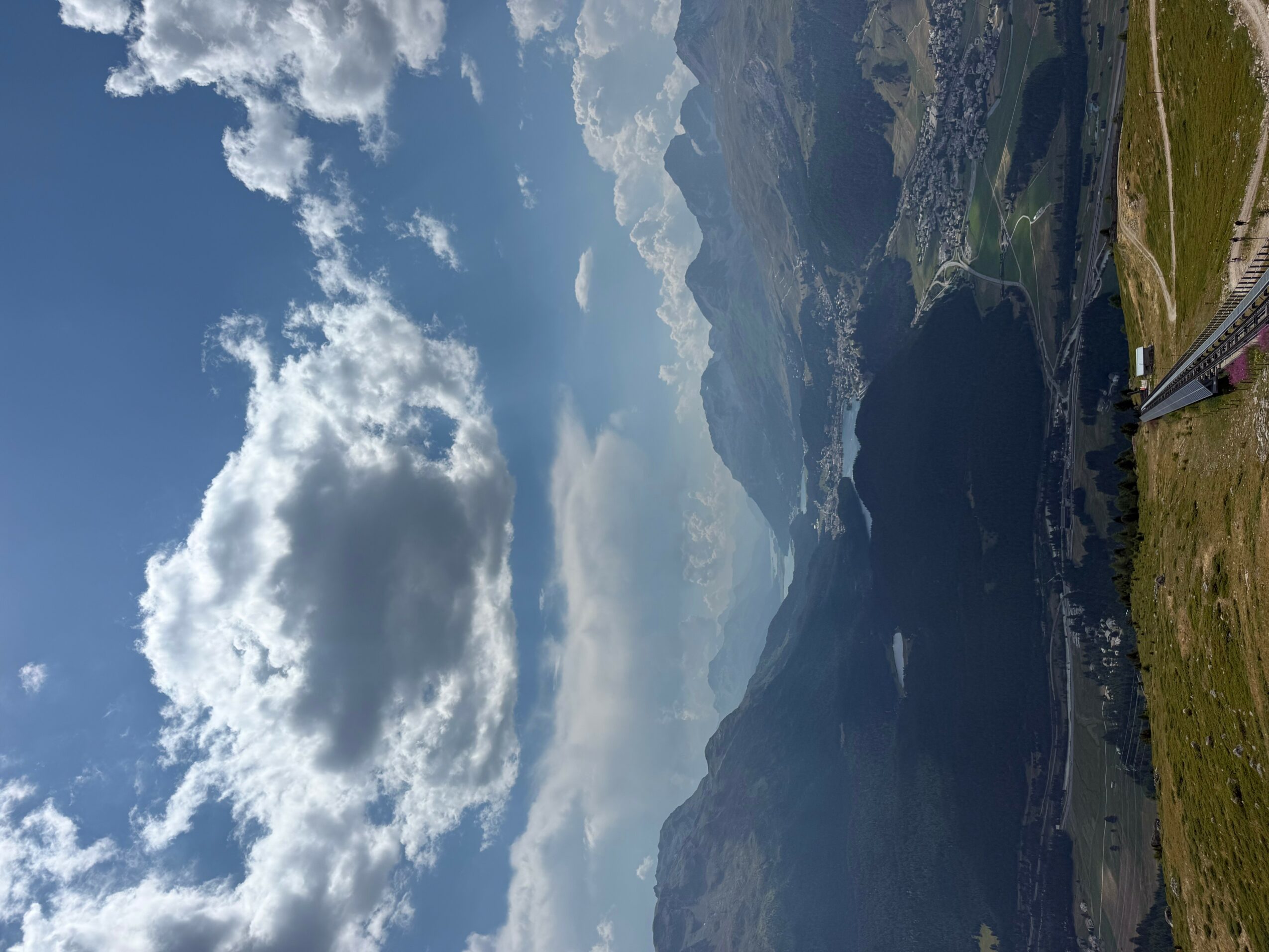 View of a lake surrounded by mountains under a partly cloudy sky, taken from an airplane window.