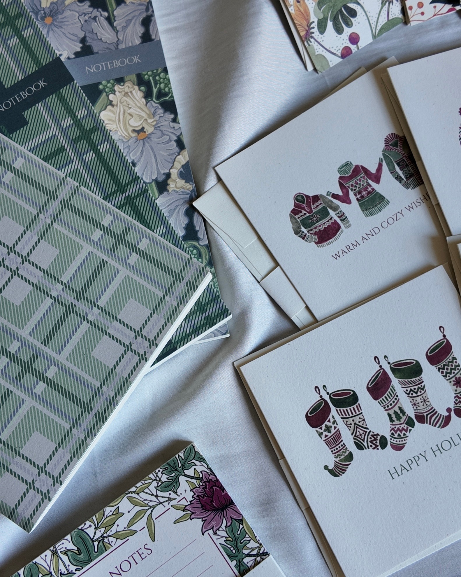 Notebooks with floral and holiday-themed designs, some with text, arranged on a white surface.